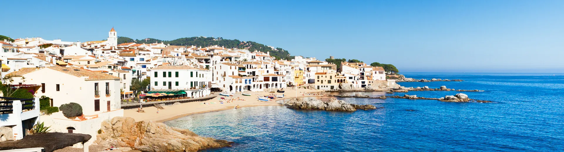 Panoramisch uitzicht op de kust van de Costa Brava in Spanje met helderblauw zeewater, rotsachtige kustlijn en een rij charmante witte en pastelgekleurde huizen langs het strand. De pittoreske baai straalt mediterrane charme uit en is ideaal voor een zonvakantie, romantische getaway of last-minute reis. Ontdek idyllische stranden, kristalhelder water en sfeervolle dorpjes in Catalonië voor een ontspannen vakantie-ervaring aan de Spaanse kust.