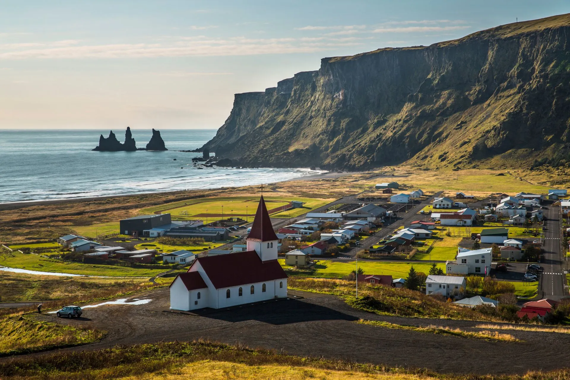 Uitzicht op het dorp Vík in IJsland, met een rode en witte kerk op de voorgrond, zwarte zandstranden en indrukwekkende kliffen op de achtergrond.