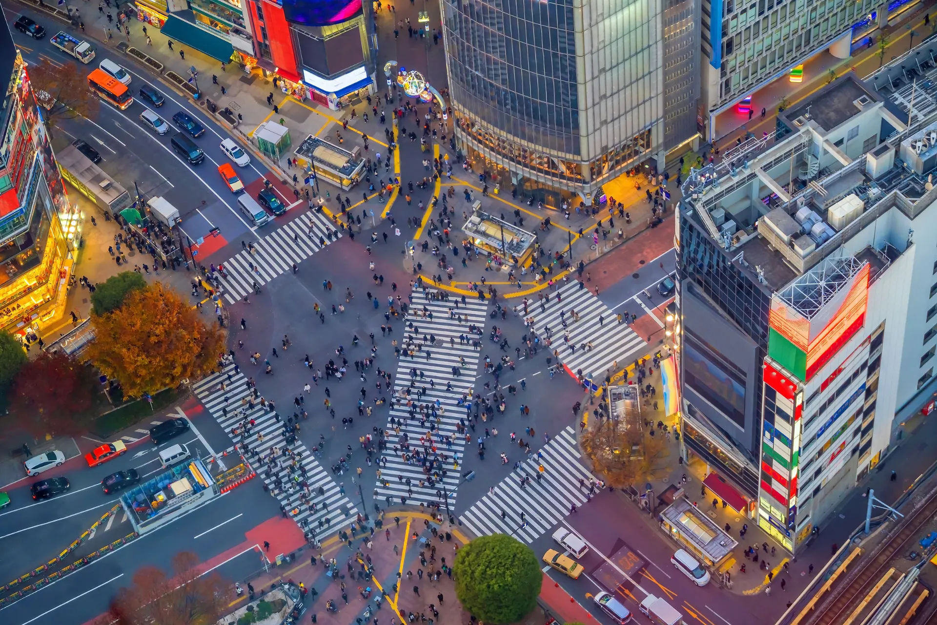 Een luchtfoto van Tokio, met drukke straten vol verkeer en opvallende zebrapaden die de stad doorkruisen. De levendige stad bruist van energie, met talloze gebouwen en mensen in beweging.