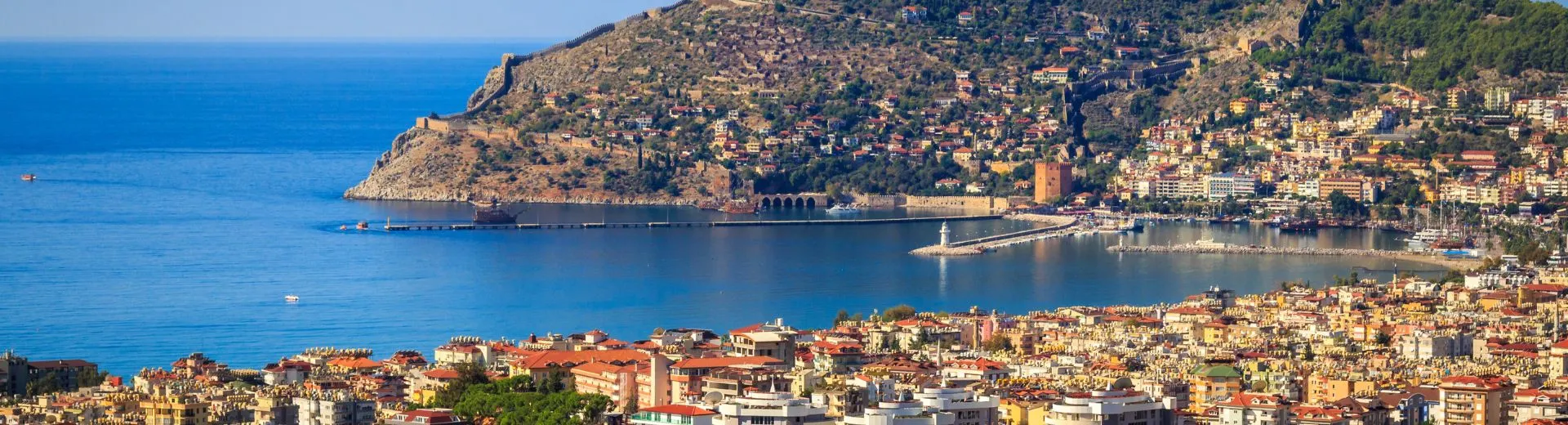 Uitzicht over Alanya aan de Turkse Rivièra met kustlijn, haven en bergen op de achtergrond. 