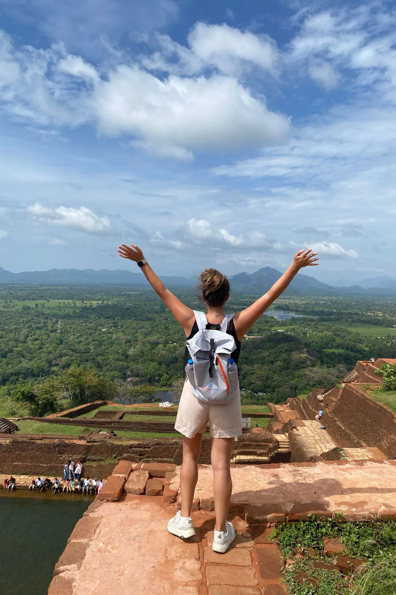 Vrouw met opgestoken armen geniet van het uitzicht vanaf de top van de Leeuwenrots in Sri Lanka.

