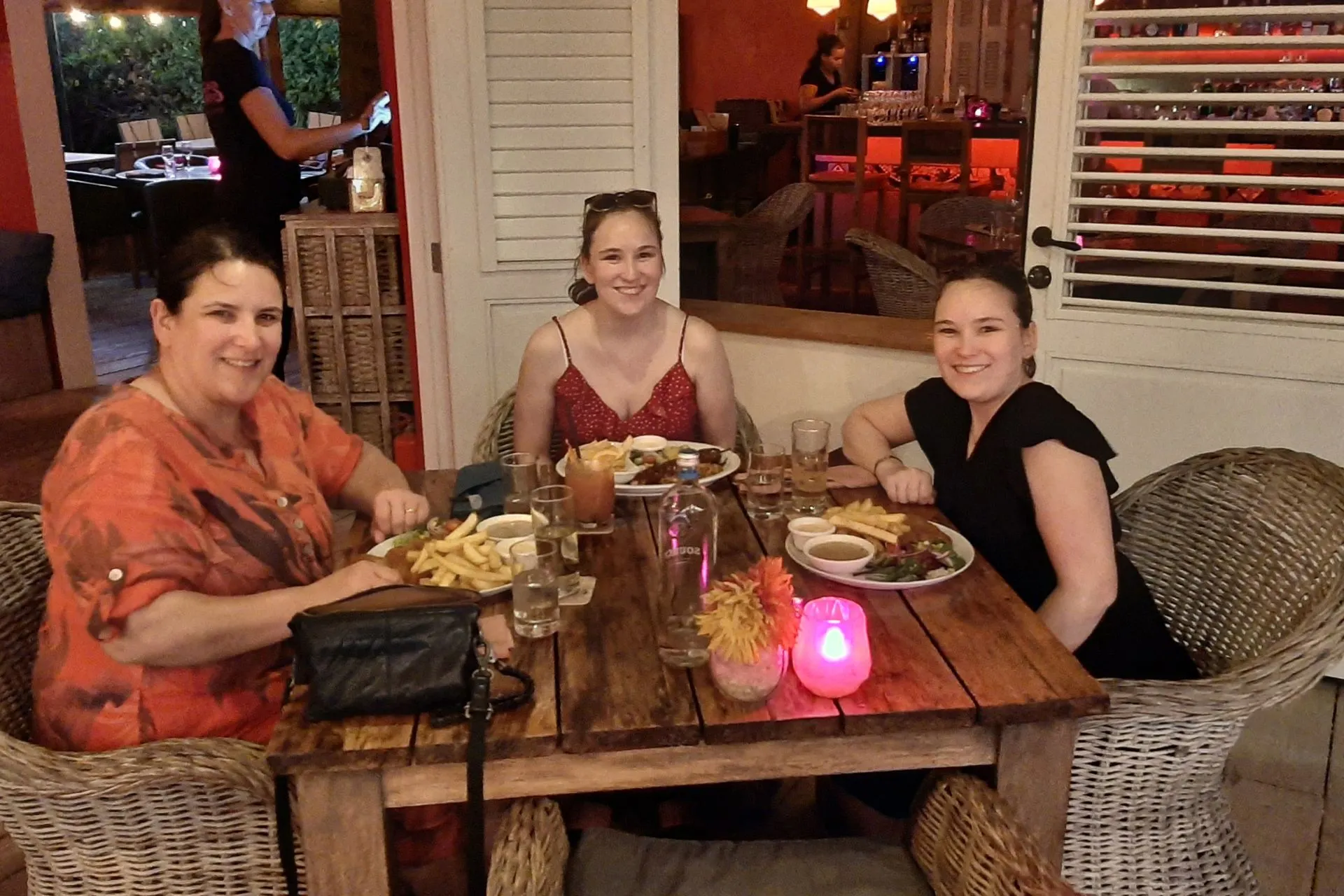 Gezellig diner in een sfeervol restaurant op Bonaire met houten tafels, kleurrijke verlichting en heerlijke gerechten zoals friet, vlees en sauzen. Bonaire biedt een breed scala aan culinaire ervaringen, van lokale specialiteiten tot internationale gerechten. De warme ambiance en tropische setting maken uit eten gaan op Bonaire een onvergetelijke ervaring. Perfect voor vakantiegangers die willen genieten van gastronomie en Caribische gastvrijheid.