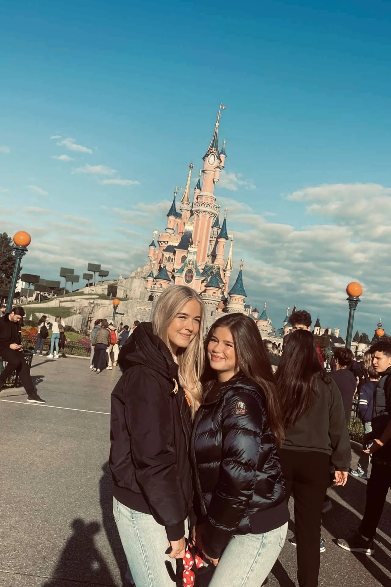 Twee bezoekers poseren op Main Street in Disneyland Parijs met het iconische Doornroosje kasteel op de achtergrond en een heldere blauwe lucht.
