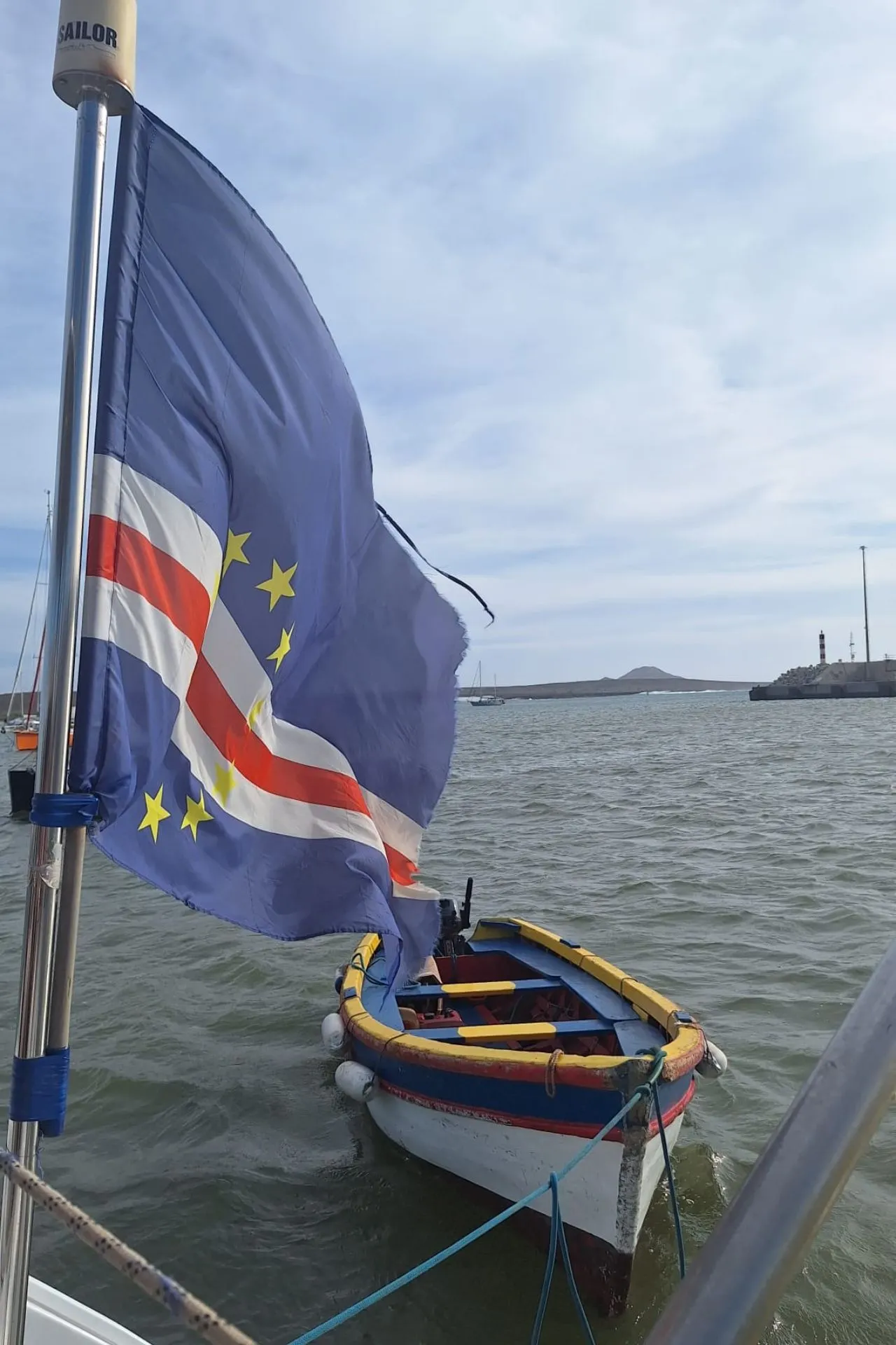 Traditionele houten boot in de haven van Kaapverdië met de Kaapverdische vlag wapperend in de wind en uitzicht op zee en kustlijn. Dit beeld weerspiegelt de maritieme cultuur van het eiland en sluit aan bij een authentieke reis Kaapverdië, waarbij lokale tradities centraal staan. Voor liefhebbers van eilandenhoppen Kaapverdië en boottochten laat deze scène zien hoe belangrijk zeevaart en visserij zijn voor het dagelijks leven op de archipel.