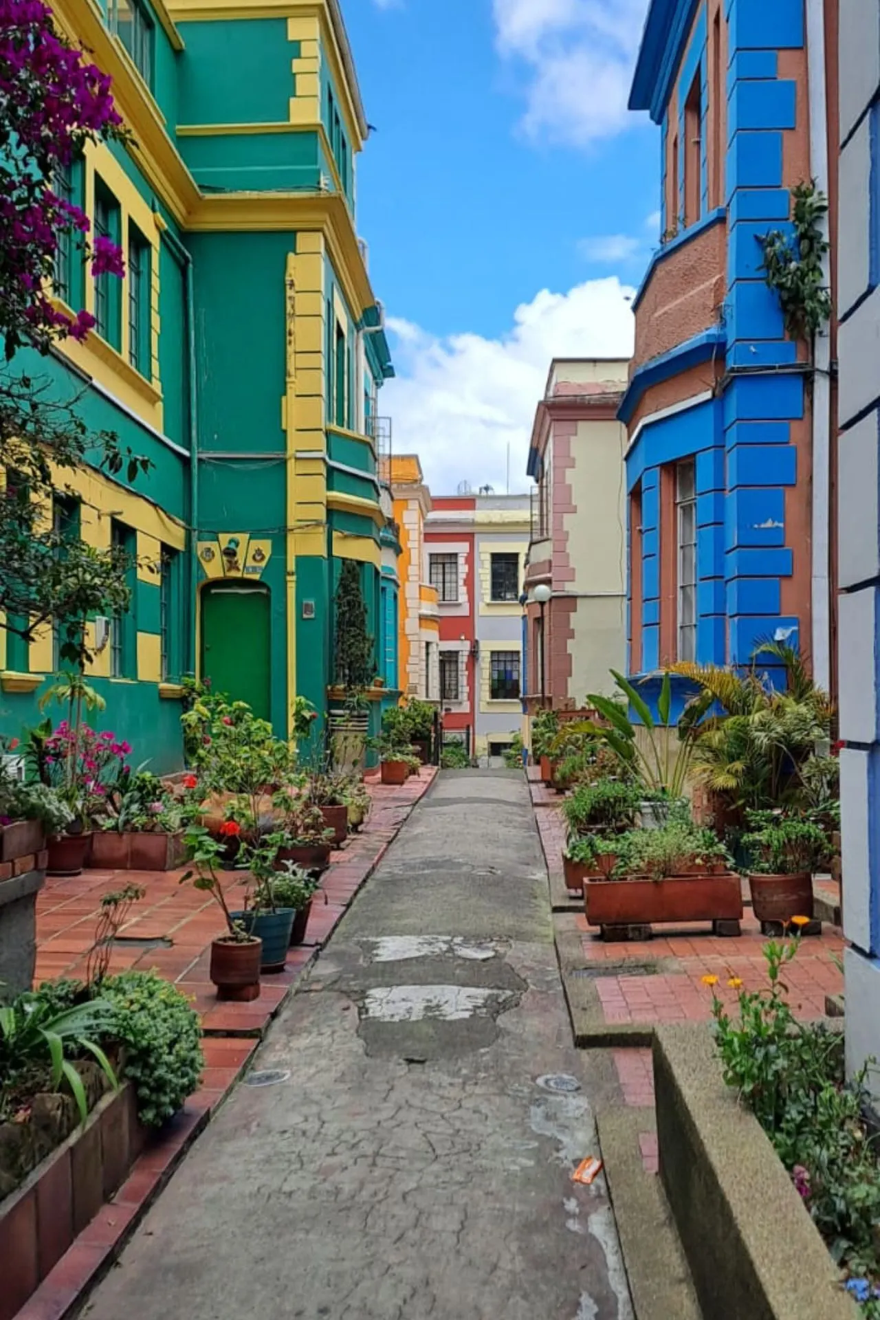Smalle doorgang tussen felgekleurde huizen in groen, geel en blauw, met bloempotten langs de randen.