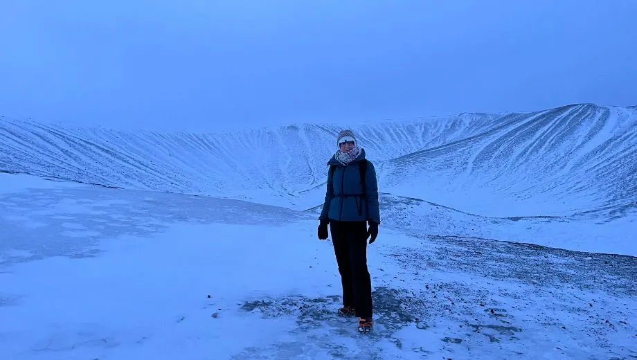 Reiziger staand voor de besneeuwde Hverfjall‑krater tijdens een winterexcursie in Noord‑IJsland.
