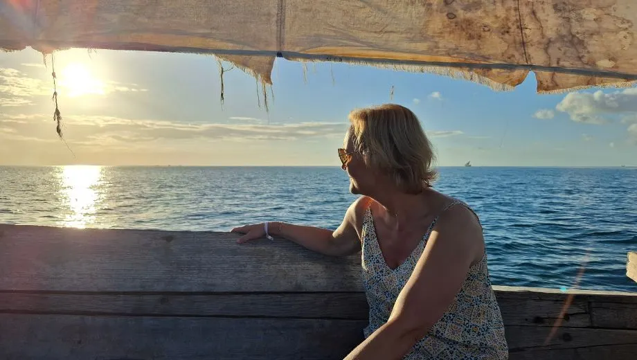 Astrid kijkt vanaf een traditionele houten dhowboot uit over de Indische Oceaan tijdens zonsondergang op Zanzibar. De rustige zee, het warme avondlicht en het uitzicht op de horizon zorgen voor een sfeervol beeld van een boottocht langs de kust van het tropische eiland Zanzibar.