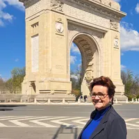 Vrouw met kort roodbruin haar en bril poseert voor een stenen boog met de Roemeense vlag op de achtergrond
