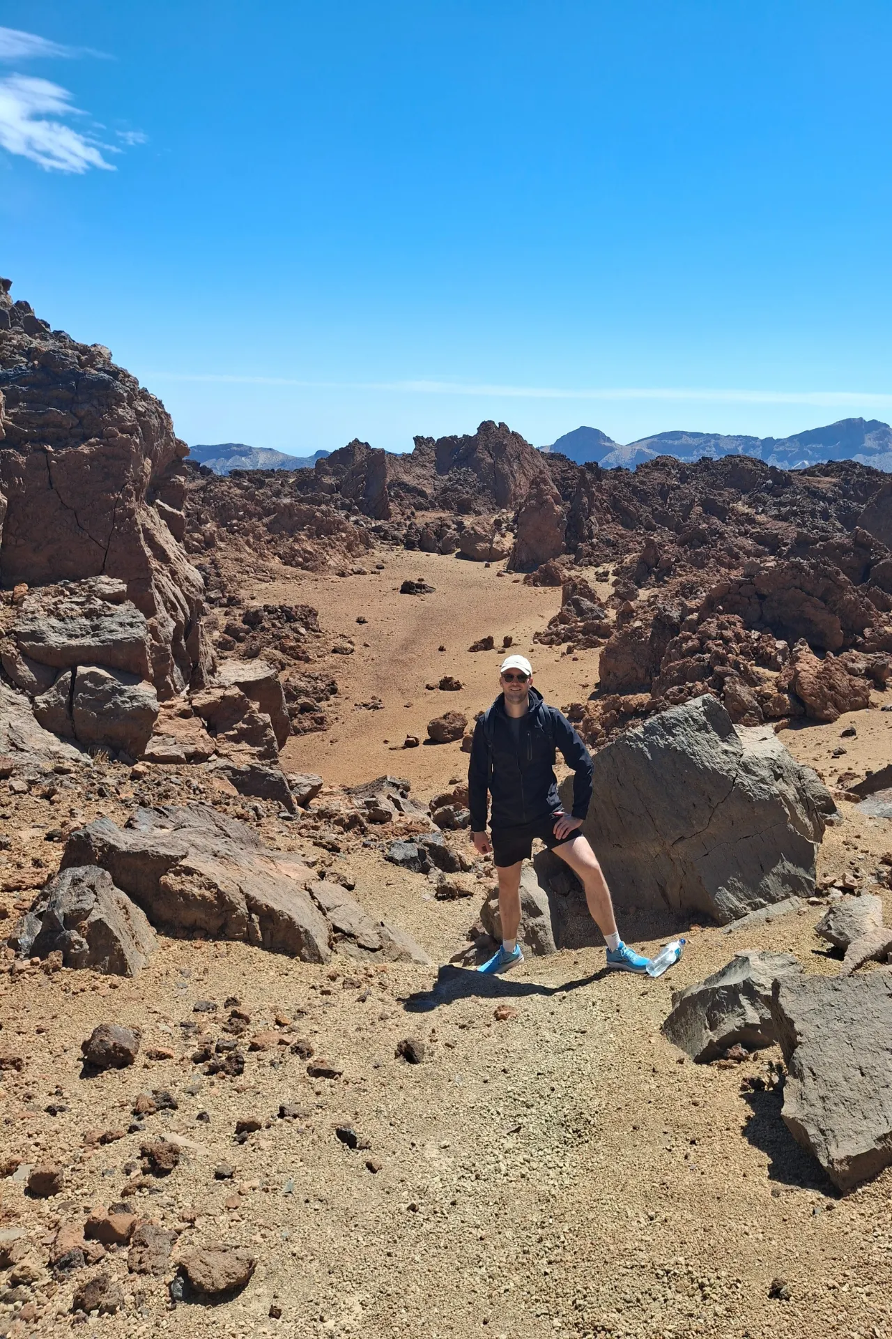 Jongen met pet staand in een zandlandschap met grote stenen, met de majestueuze Teide vulkaan op de achtergrond in Tenerife.