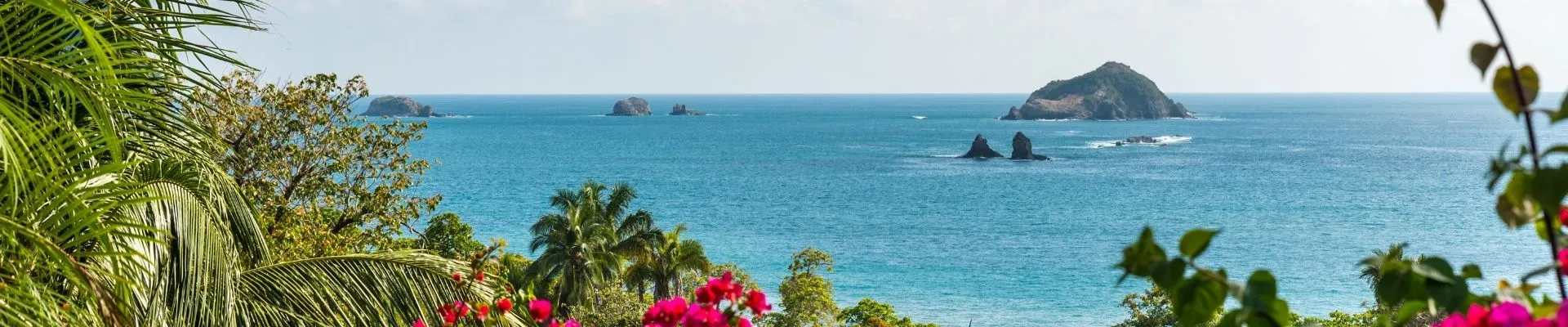 Uitzicht over de tropische kust van Costa Rica met azuurblauwe oceaan, groene palmbomen en kleine eilandjes voor de kust. Deze paradijselijke omgeving laat de veelzijdigheid van Costa Rica zien, waar natuur, stranden en avontuur samenkomen. 