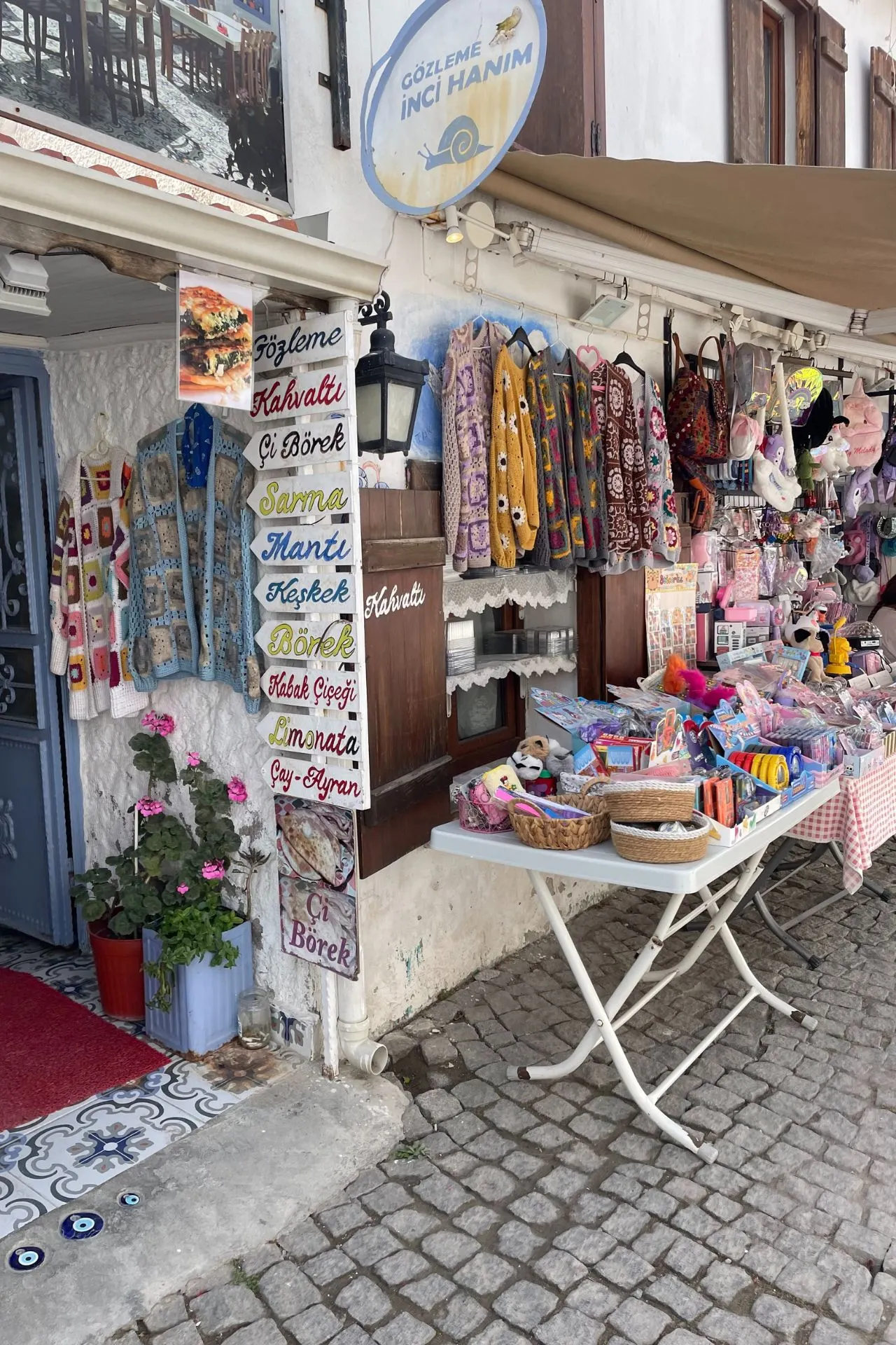 Kleinschalig winkeltje in Sığacık met kleurrijke kleding, speelgoed en een bord vol gerechten als gözleme en börek.
