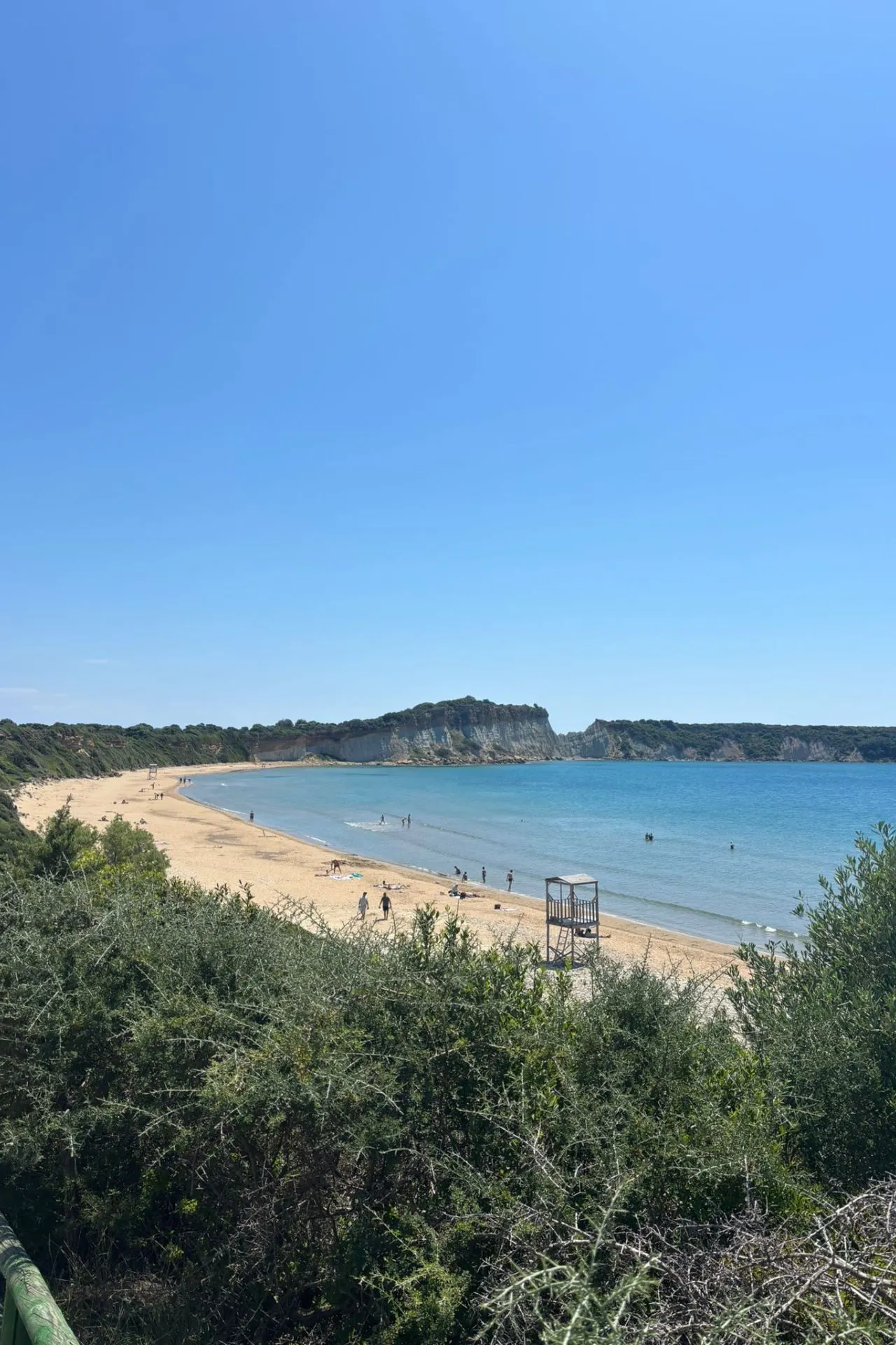 Breed zandstrand met helderblauwe zee en enkele badgasten op Zakynthos, perfect voor een ontspannen dag.