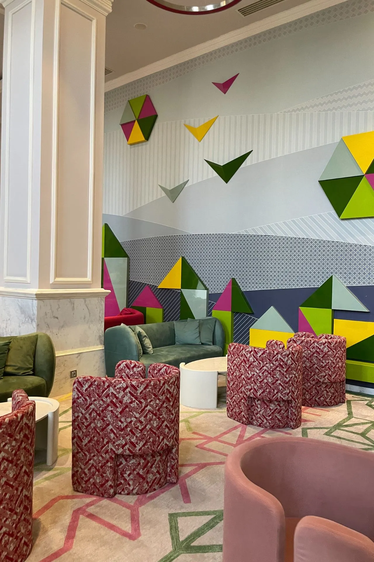 Binnenruimte van het hotel met groene accenten, grote open ruimte en decoratieve elementen zoals lampen en speelse vormen.