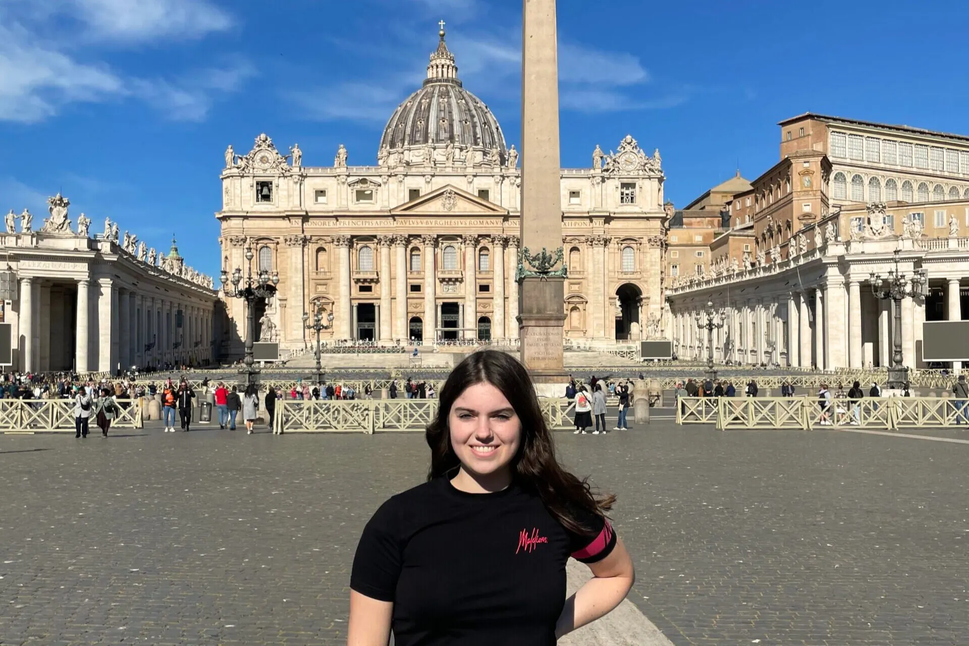 Lachende vrouw met bruin haar poseert voor de Sint-Pieterskerk in Rome op een zonnige dag.