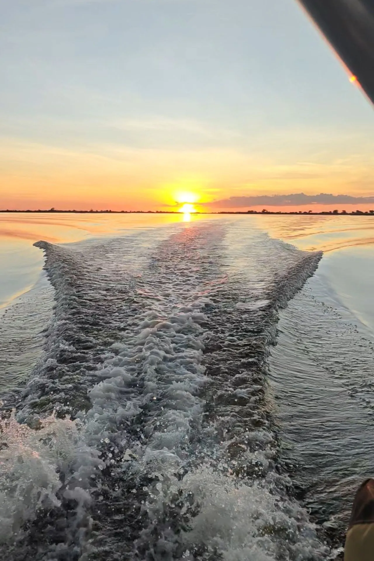Achterkant van de boot met uitzicht op het water, omgeven door warm oranje en rode tinten van de zonsondergang
