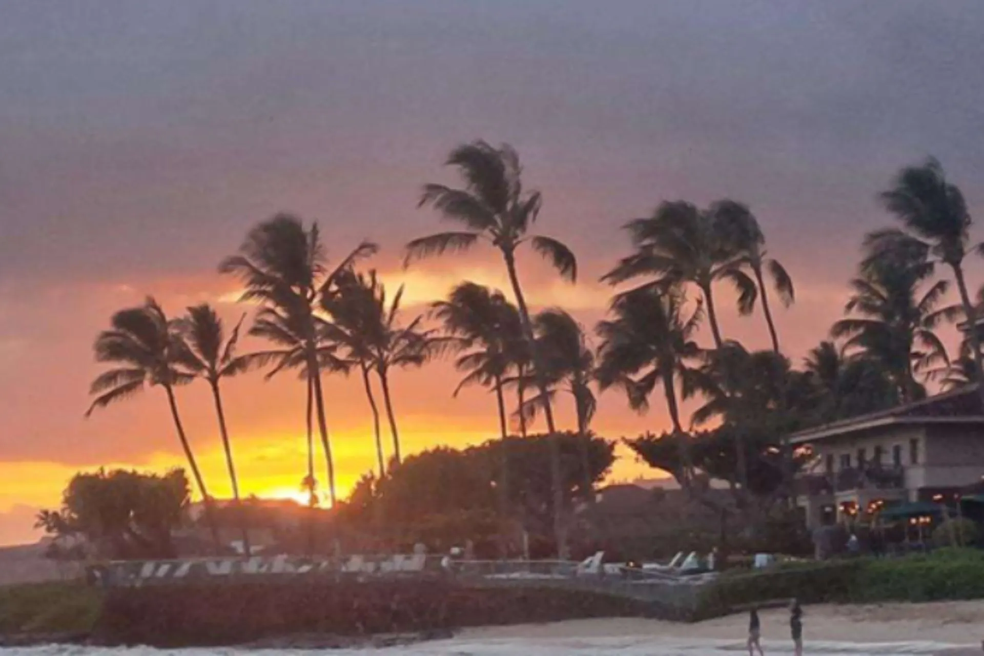 Tropische zonsondergang bij Poipu Beach op Kauai, met wuivende palmbomen en warme kleuren aan de horizon