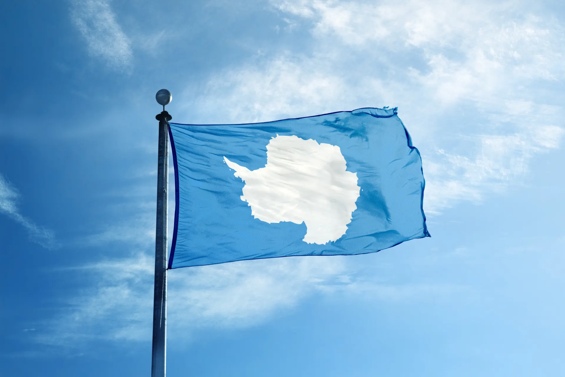 Wapperende vlag van Antarctica tegen een helderblauwe lucht.