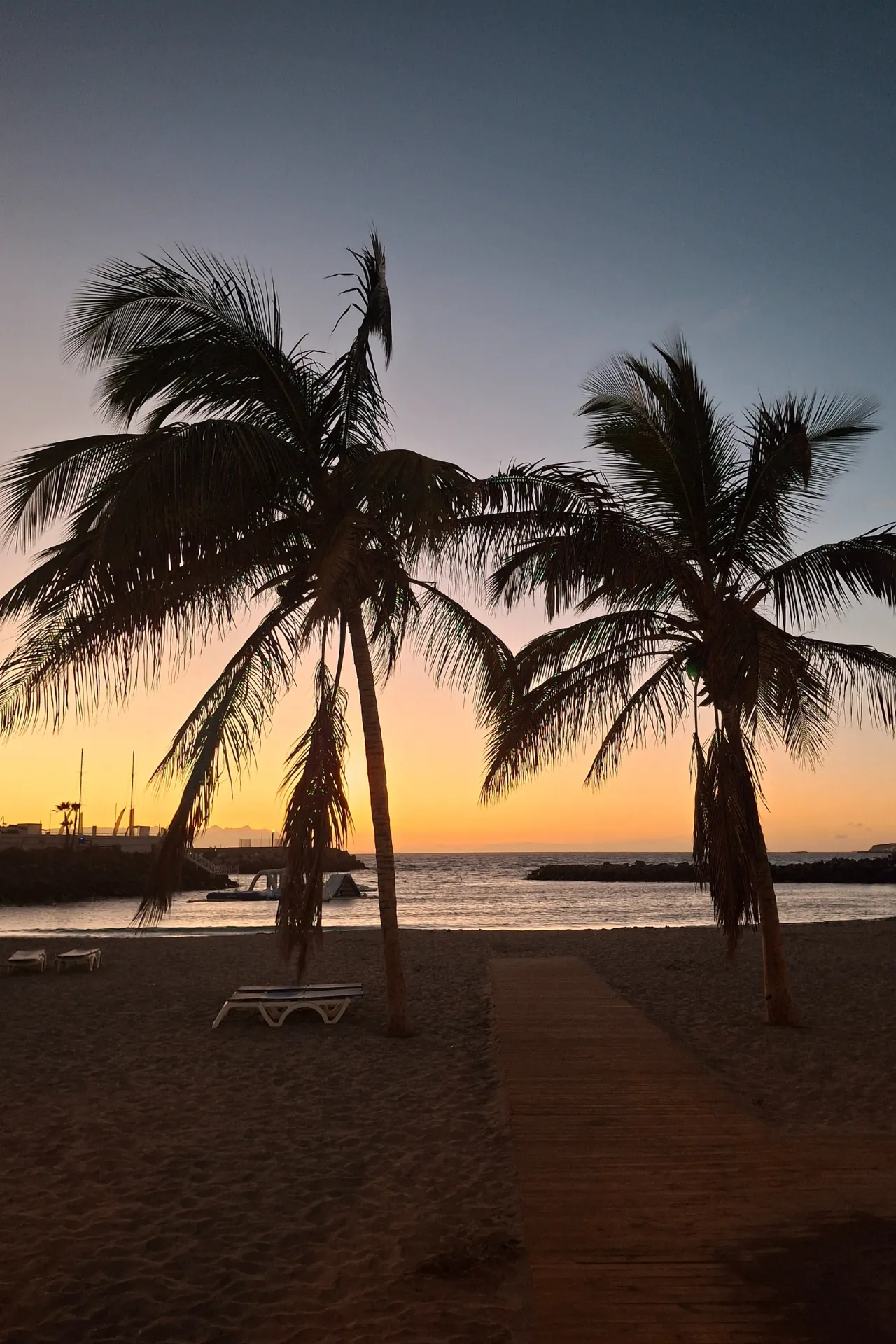 Zonsondergang bij het strand van Costa Adeje, met palmbomen en een warme oranje gloed in de lucht.