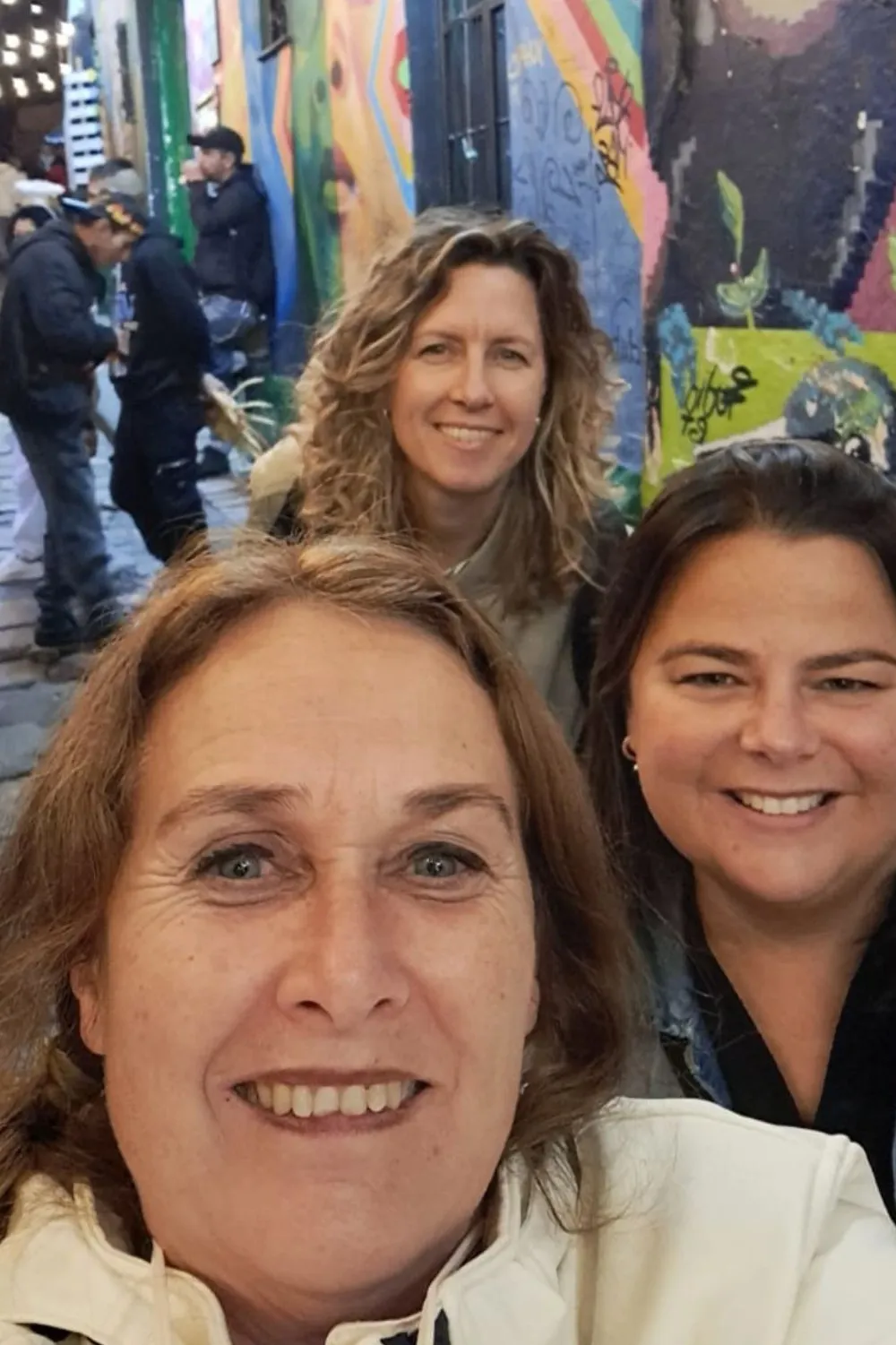 Smalle straat met kleurrijke muurschilderingen en lichtslingers, mensen wandelen en staan langs de muren in een levendige steeg.