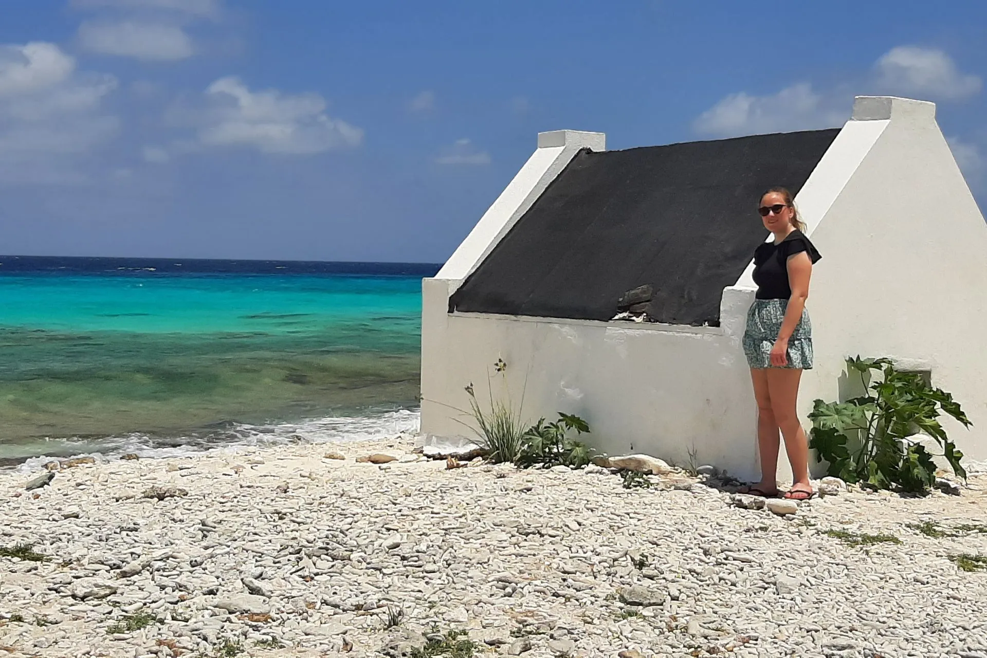 Wit slavenhuisje op Bonaire direct aan de kust met turquoise zee en witte kiezels op de voorgrond. Dit historische gebouw is een belangrijk monument dat het slavernijverleden van het eiland symboliseert. De locatie biedt een prachtig uitzicht op de Caribische zee en is populair bij toeristen die cultuur en natuur willen combineren. Bonaire staat bekend om zijn unieke mix van geschiedenis, stranden en helderblauw water, ideaal voor educatieve en ontspannende trips.