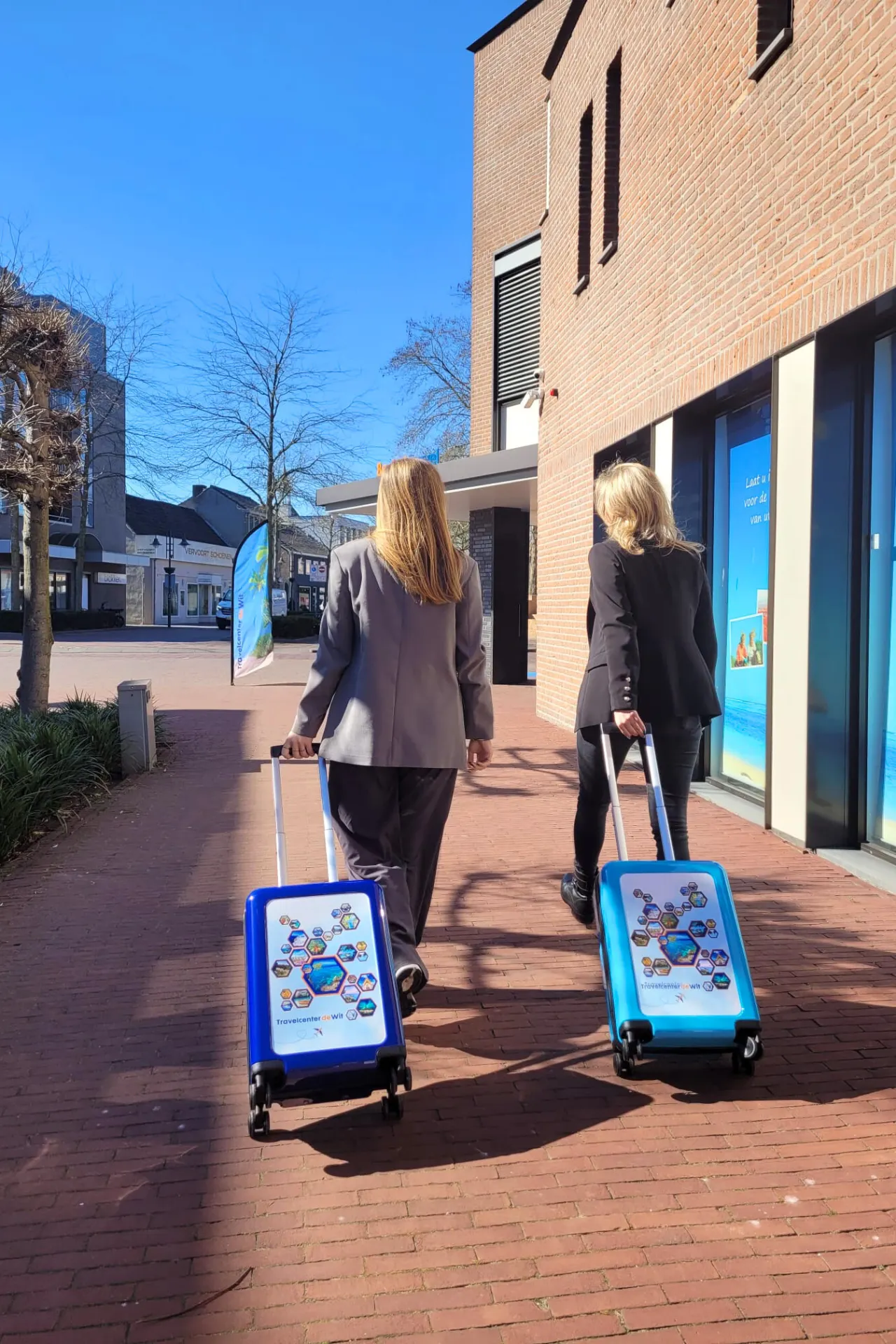  Martje en Manon lopen met twee reistrolleys van Travelcenter de Wit, klaar voor hun reis.