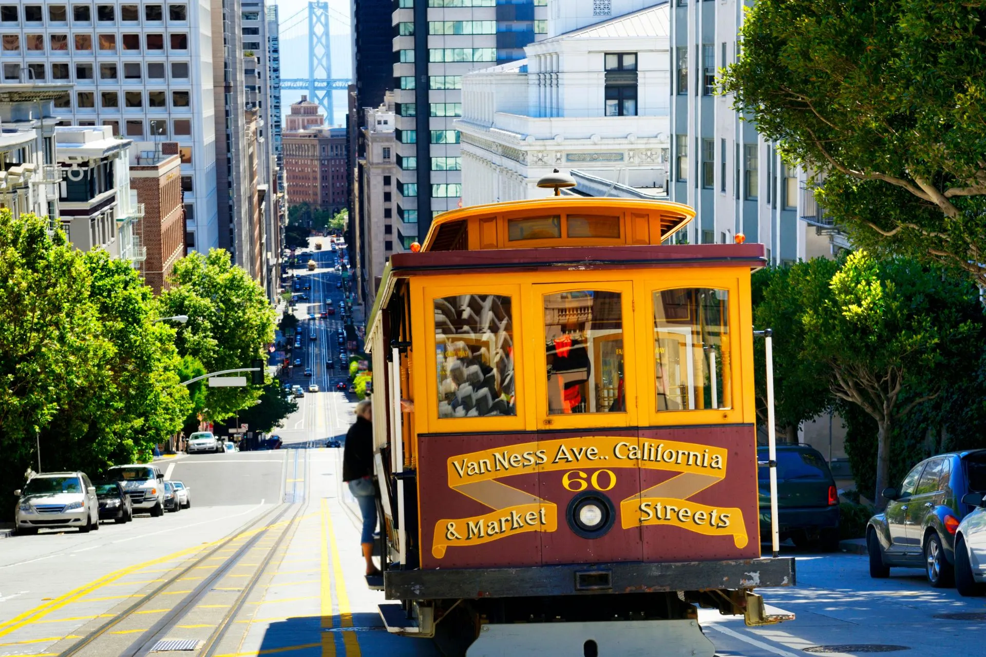 Kabeltram in San Francisco op een steile straat met uitzicht op de Bay Bridge en omliggende gebouwen – iconisch stadsbeeld.