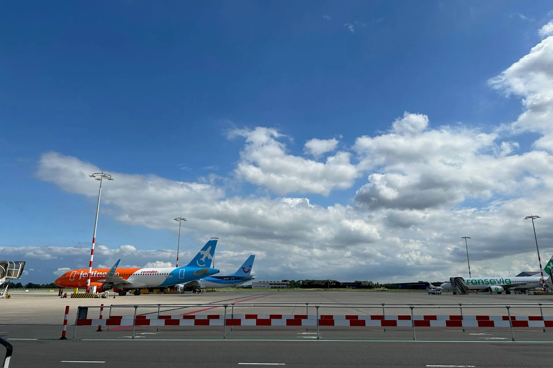 Twee vliegtuigen, in de kleuren rood, wit en blauw staan klaar op de landingsbaan onder een stralend blauwe lucht. Ervaar het gemak van vliegen vanaf Rotterdam met diverse vluchten vanaf Rotterdam Airport en een snelle, comfortabele vertrek vanaf Luchthaven Rotterdam.