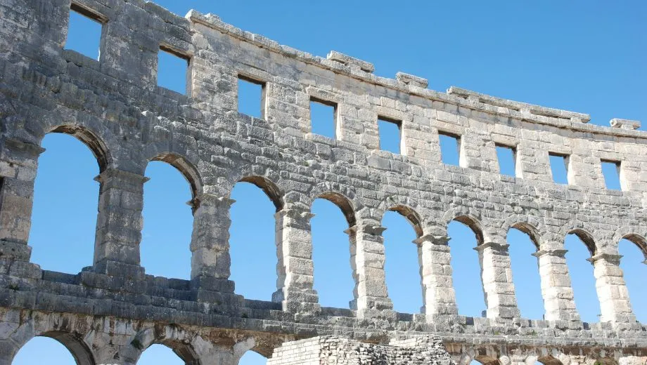 "Detail van het beroemde Romeinse amfitheater in Pula, Istrië, Kroatië, met imposante stenen bogen tegen een heldere blauwe lucht. Dit historische monument is een van de best bewaarde amfitheaters ter wereld en een topattractie in Istrië. Perfect voor liefhebbers van cultuur, geschiedenis en architectuur. Ontdek Pula’s rijke erfgoed, mediterrane sfeer en bezienswaardigheden tijdens een vakantie in Kroatië."