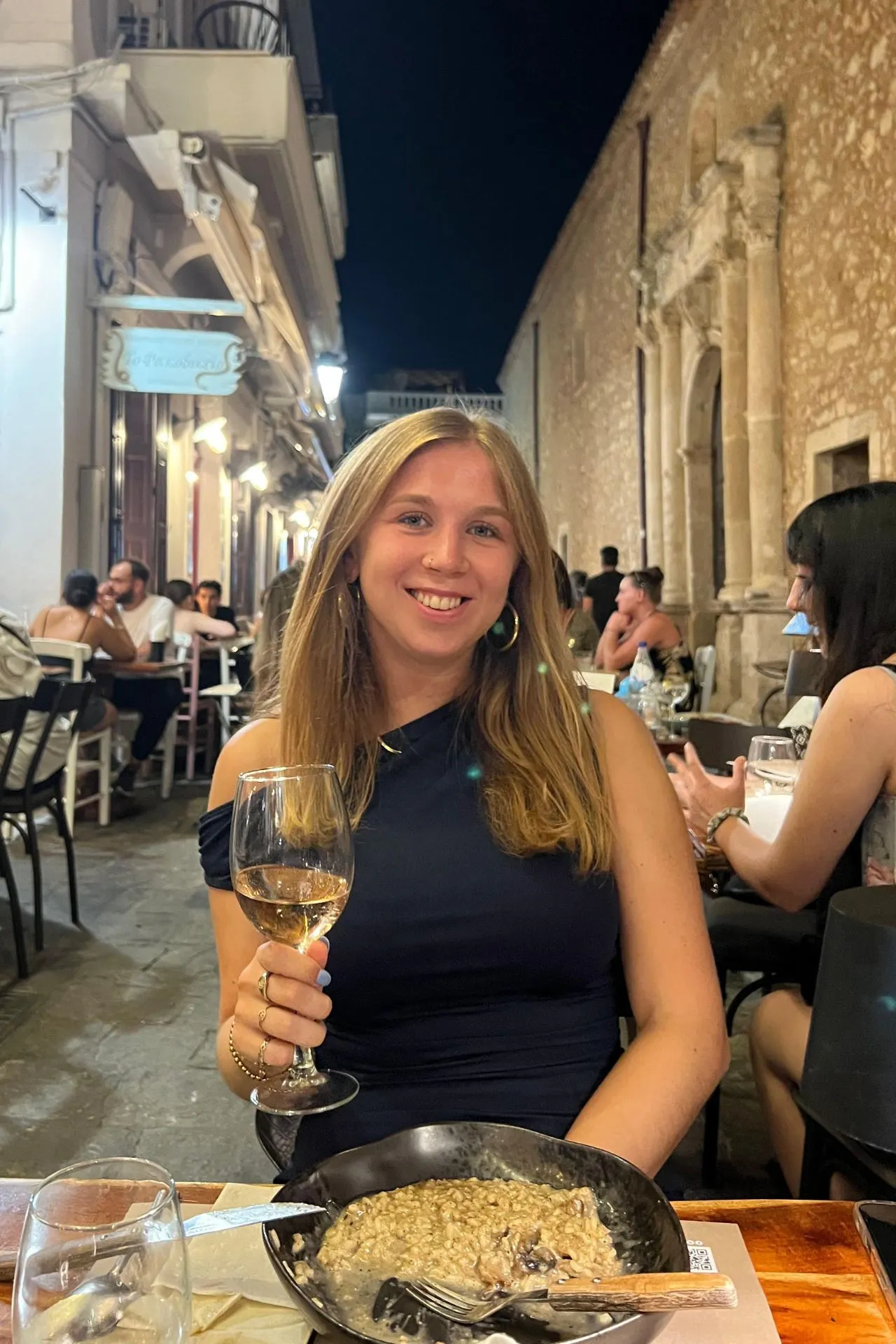 Vrouw dineert met een glas rosé aan een sfeervolle tafel in de oude binnenstad van Rethymnon, omringd door historische gebouwen en gezellige terrassen.