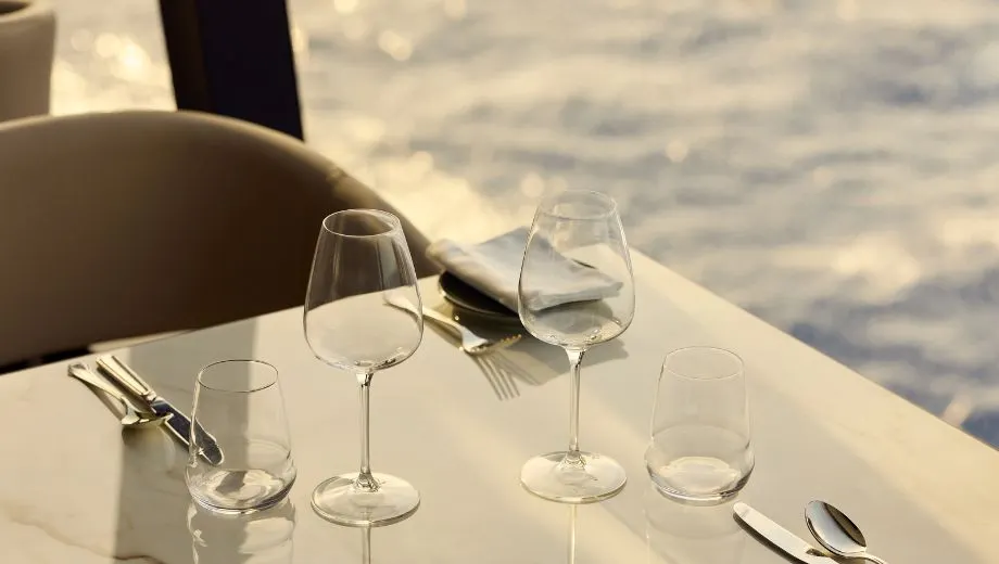 Elegante gedekte tafel aan boord van een Explora Cruise schip, met luxe wijnglazen, bestek en een prachtig uitzicht op de oceaan door het raam. Deze foto benadrukt de verfijnde culinaire ervaring en stijlvolle ambiance die Explora Journeys biedt tijdens een premium cruisevakantie. Geniet van gastronomische gerechten, exclusieve service en een serene setting op zee, ideaal voor reizigers die op zoek zijn naar luxe en comfort tijdens hun cruise.