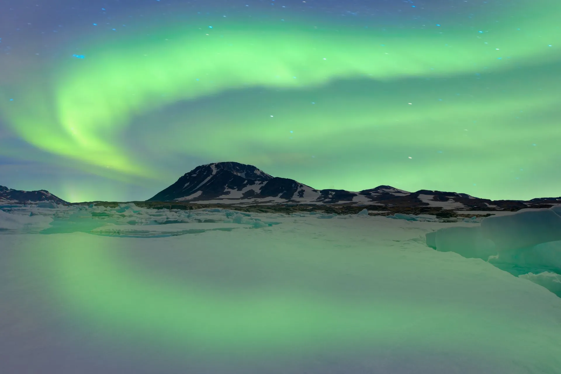 Het noorderlicht danst boven een besneeuwd berglandschap in Groenland, met ijsformaties en een mysterieuze groene gloed in de lucht.