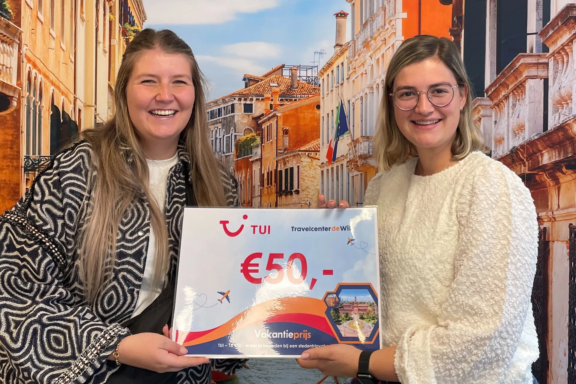 Twee vrouwen lachen met een TUI-voucher van €50 tijdens de prijsuitreiking van de winactie bij Travelcenter de Wit Gemert.