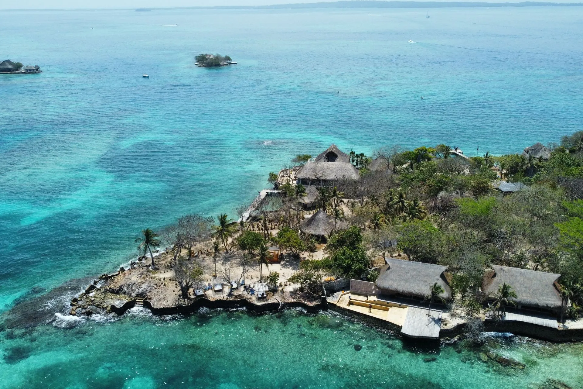 Turquoise water met heldere blauwgroene tinten omsluit een afgelegen tropisch eiland met luxe strandlodges en rieten daken, omringd door palmbomen, rotsen en ongerepte natuur. Het idyllische landschap straalt rust, exclusiviteit en Caribische charme uit en past perfect bij de ontspannen sfeer van een ultra-luxe cruise of een hotelbeleving op zee, waar reizigers genieten van privacy, paradijselijke stranden en betoverende eilanduitzichten.