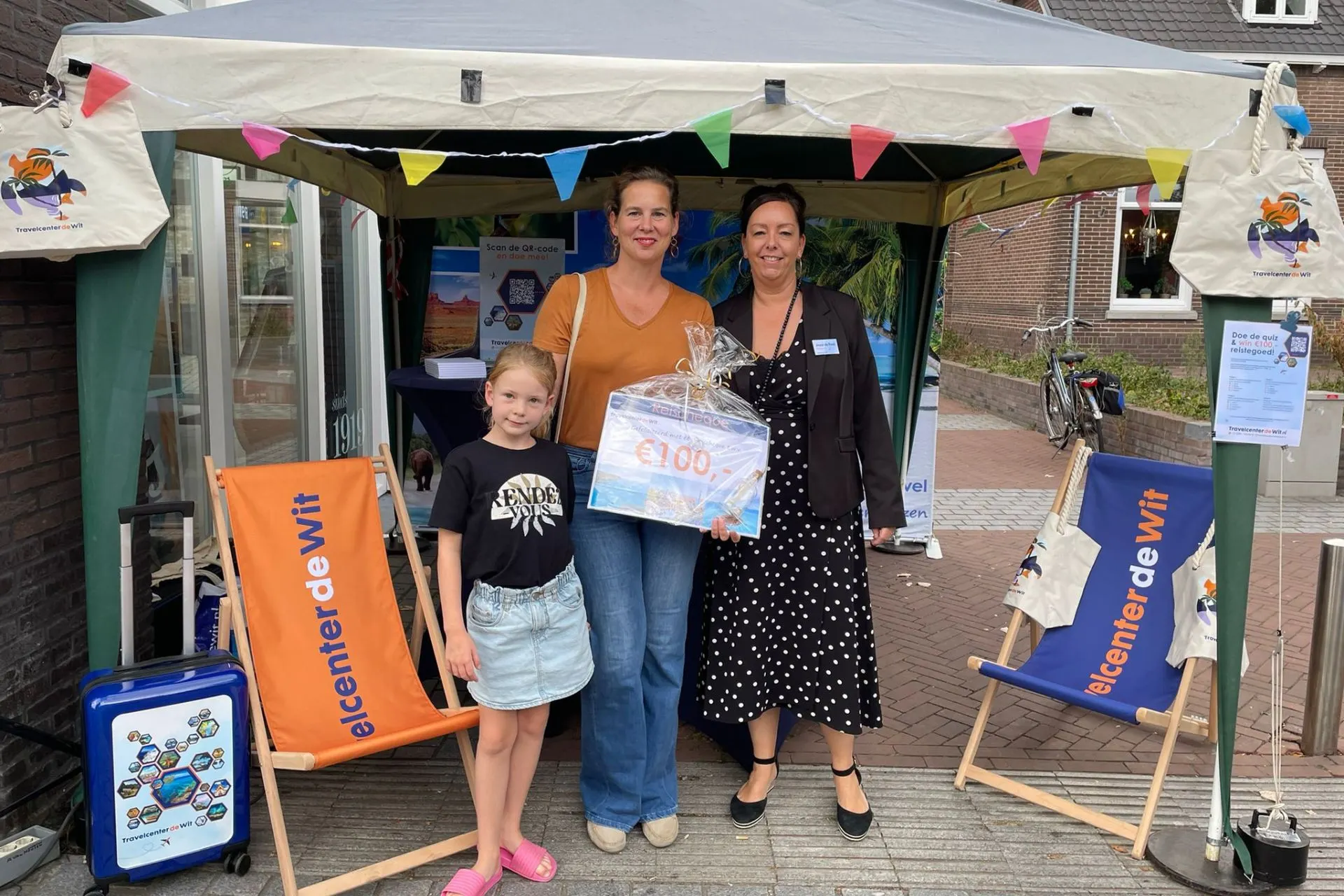 Winnares van de reischeque van €100 met haar dochter en een medewerker van Travelcenter de Wit bij de promotiekraam tijdens Thuis in Rosmalen 2025.