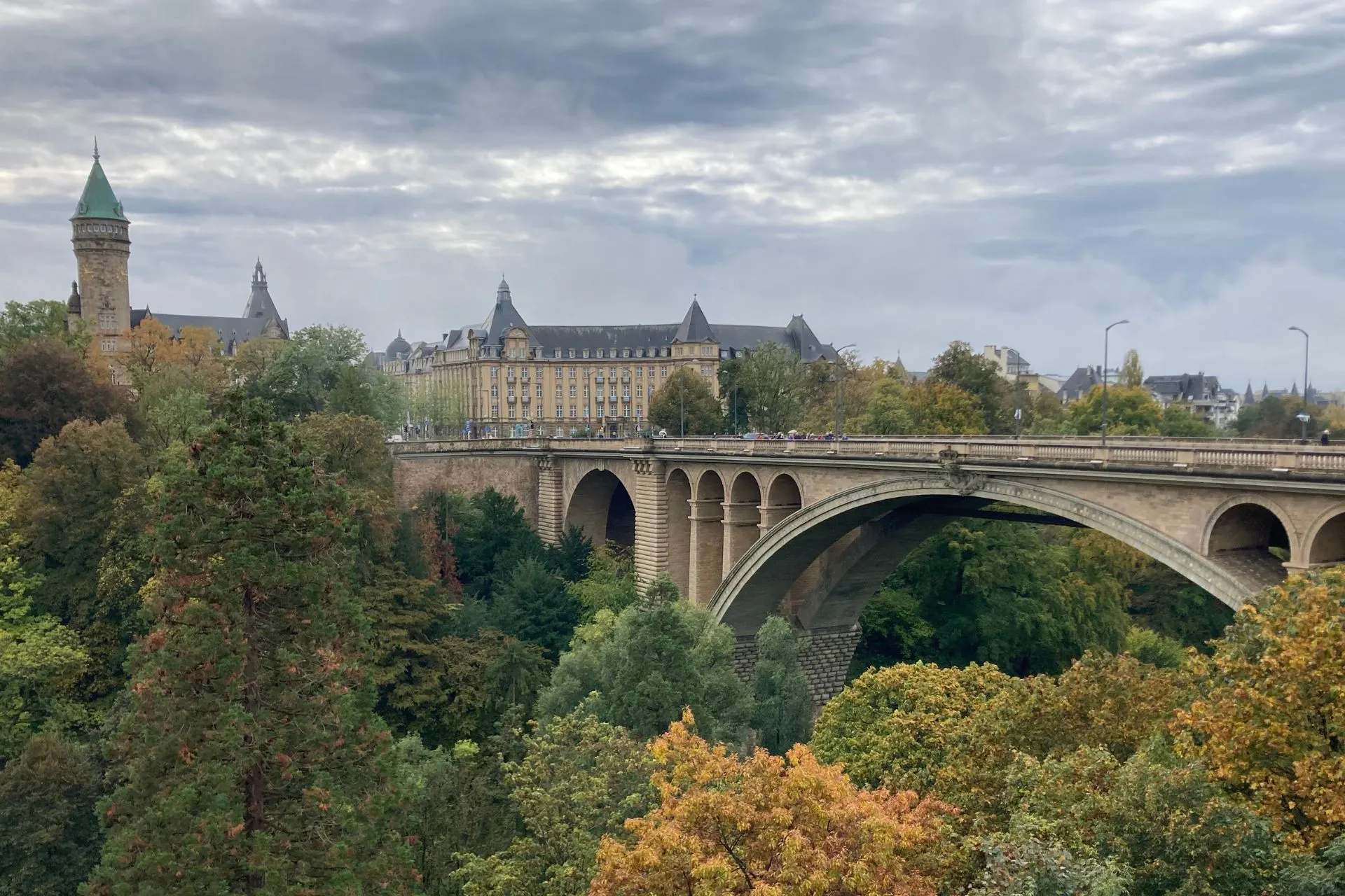 Panoramisch uitzicht op een historische brug en omliggende gebouwen in Luxemburg Stad, omringd door groene bomen en een bewolkte lucht