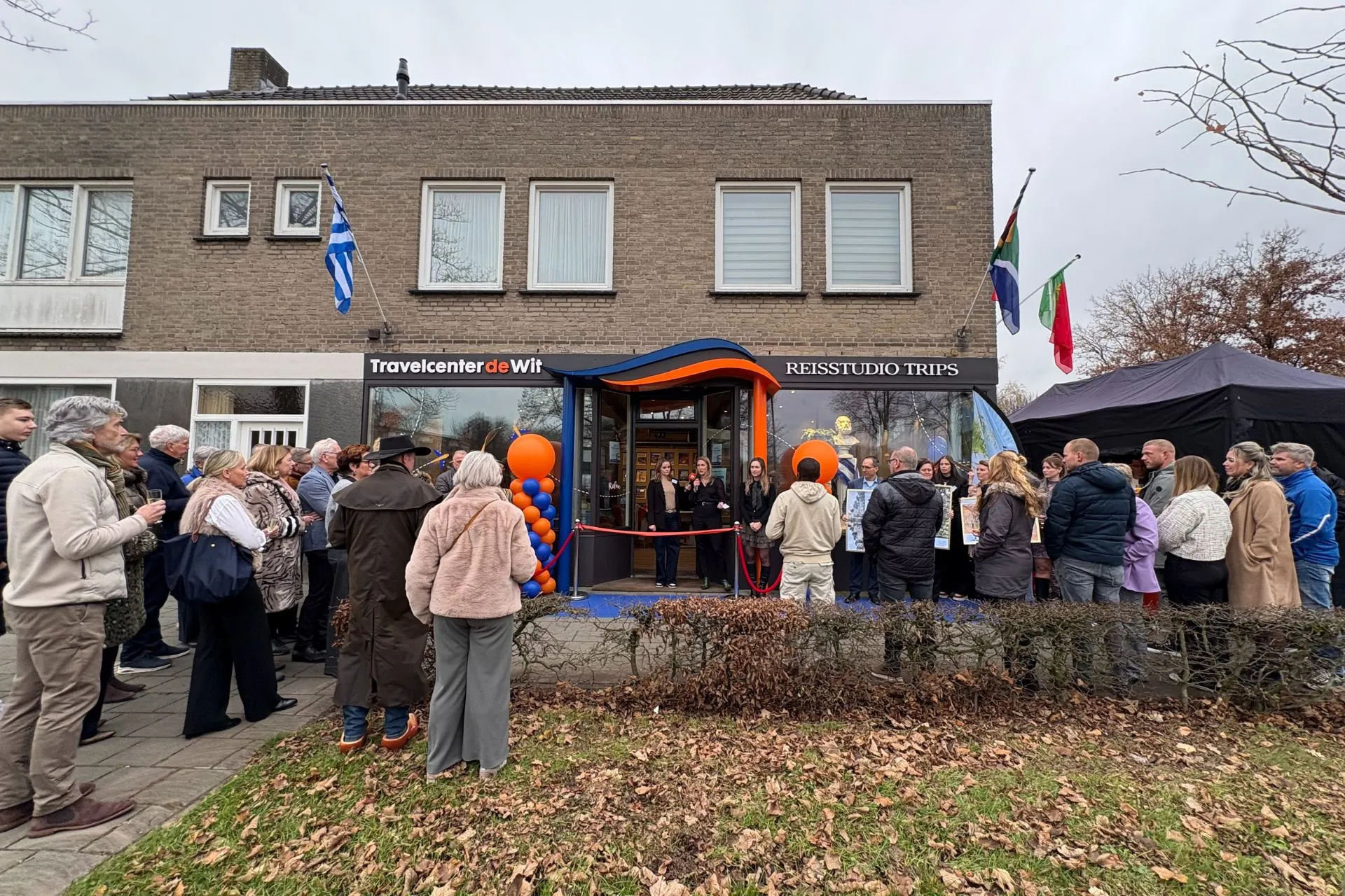 Groep bezoekers verzameld voor het vernieuwde filiaal Travelcenter de Wit Asten tijdens het officiële openingsmoment, met ballonnen en vlaggen bij de entree.