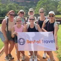 Groepsfoto van zeven lachende reisprofessionals tijdens een studiereis in Sri Lanka, georganiseerd door Best of Travel. De deelnemers poseren op een zonnige locatie met een groen landschap en historische ruïnes op de achtergrond. Ze houden samen een banner vast met het logo van Best of Travel. De sfeer is ontspannen en enthousiast, passend bij een leerzame en inspirerende reiservaring.