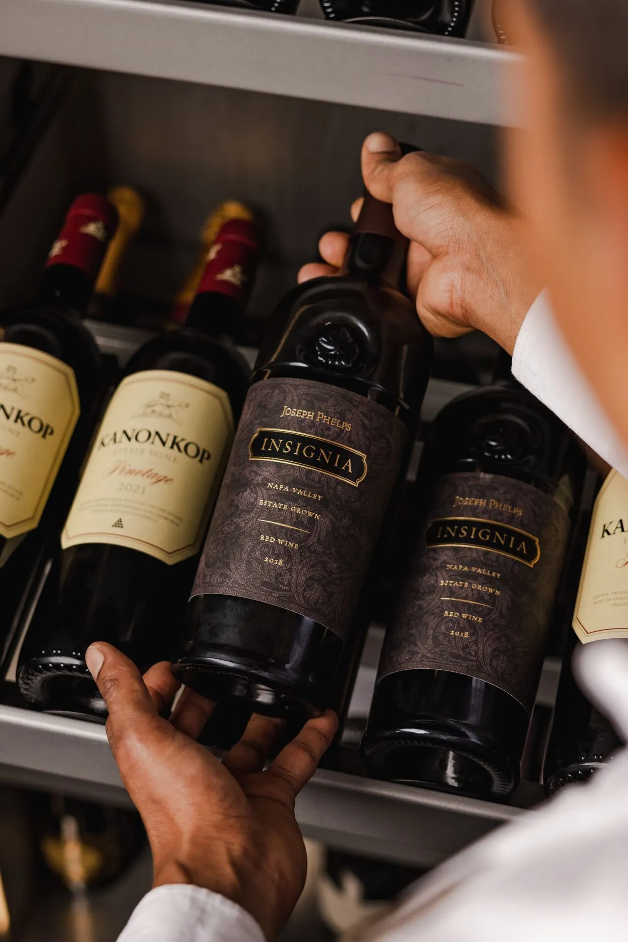 Close-up van een luxe wijnselectie aan boord van een Explora Cruise, waarbij een medewerker een fles Insignia rode wijn presenteert uit een elegante wijnkast. Deze afbeelding benadrukt de verfijnde culinaire ervaring en exclusieve service die Explora Journeys biedt tijdens een premium cruisevakantie. Ontdek hoogwaardige wijnen, gastronomische gerechten en persoonlijke aandacht op zee, ideaal voor liefhebbers van luxe reizen en unieke bestemmingen.