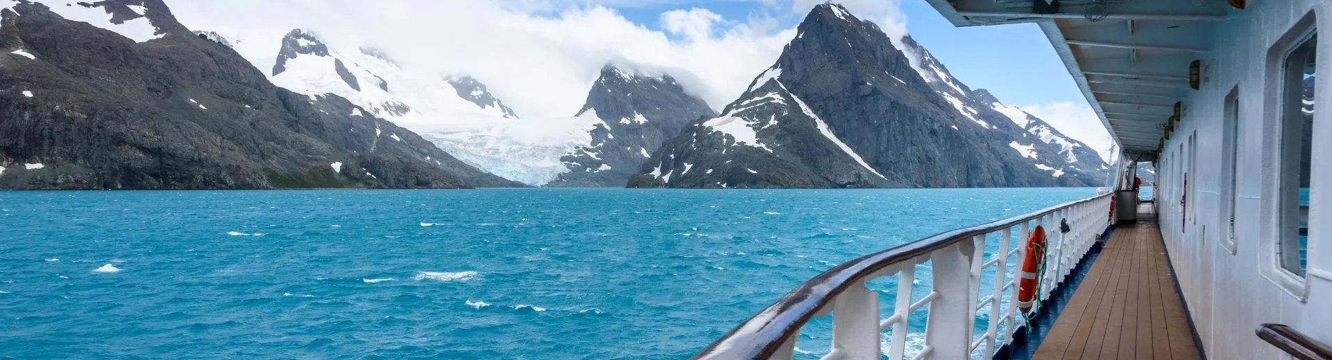 Cruiseschip varend door indrukwekkend berg- en fjordenlandschap met uitzicht vanaf het dek. Een cruisevakantie combineert comfort, ontspanning en unieke bestemmingen, waarbij je meerdere landen bezoekt terwijl je geniet van luxe faciliteiten aan boord.