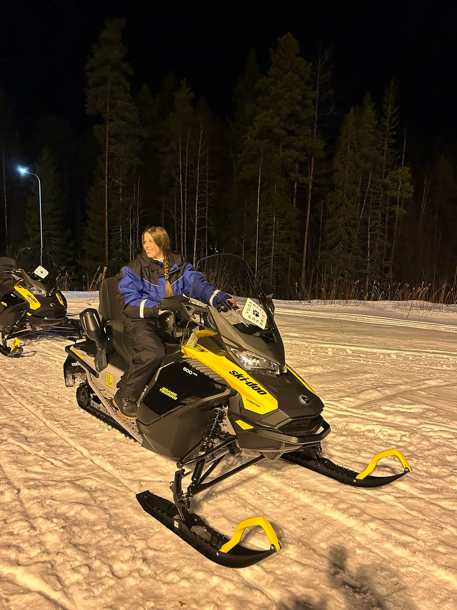 Dame met bruine lange haren en een blauwe jas op een sneeuwscooter in Arctic lakeland Finland.