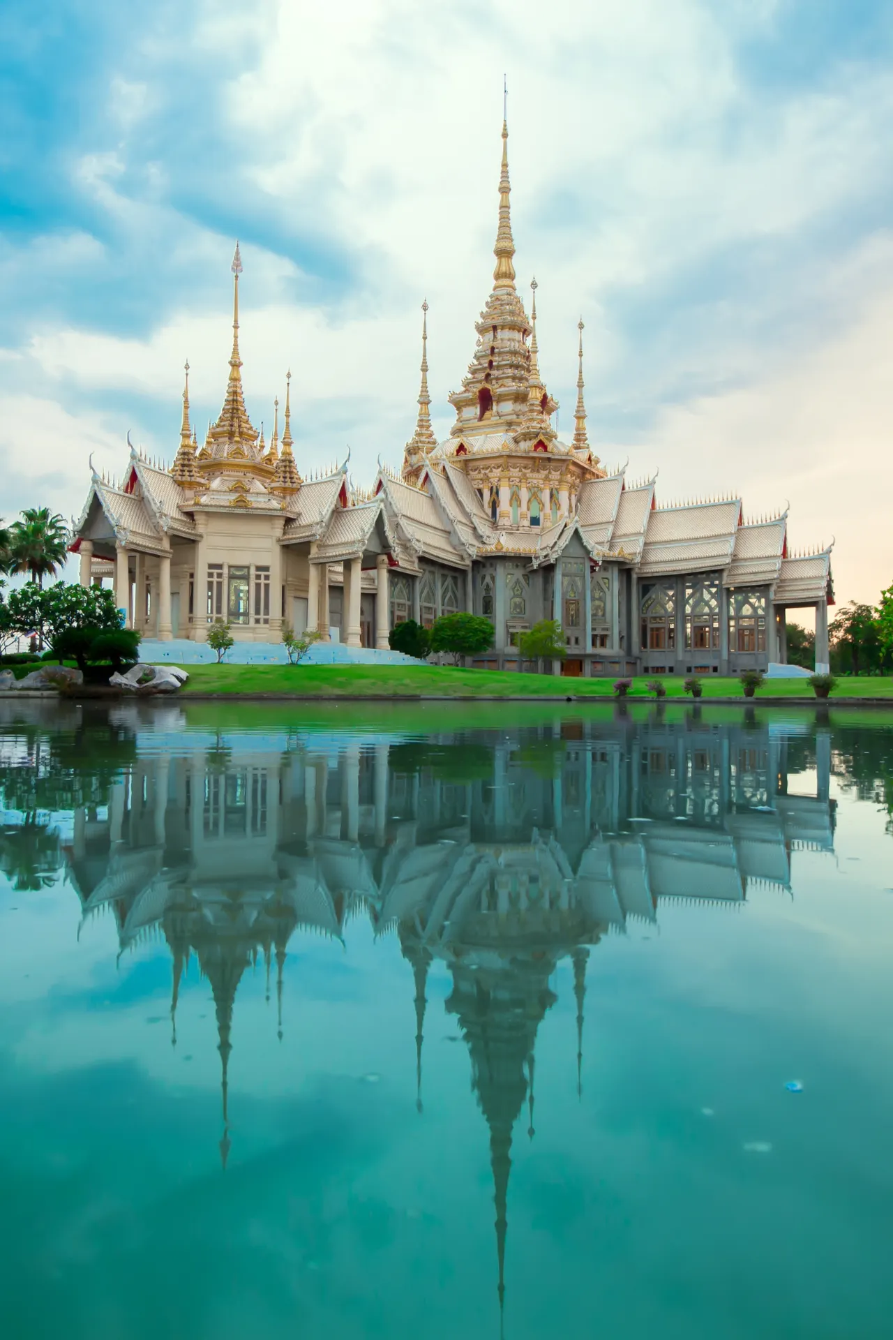 Beige Thaise tempel met sierlijke daken, weerspiegeld in het rustige water aan de voorzijde.