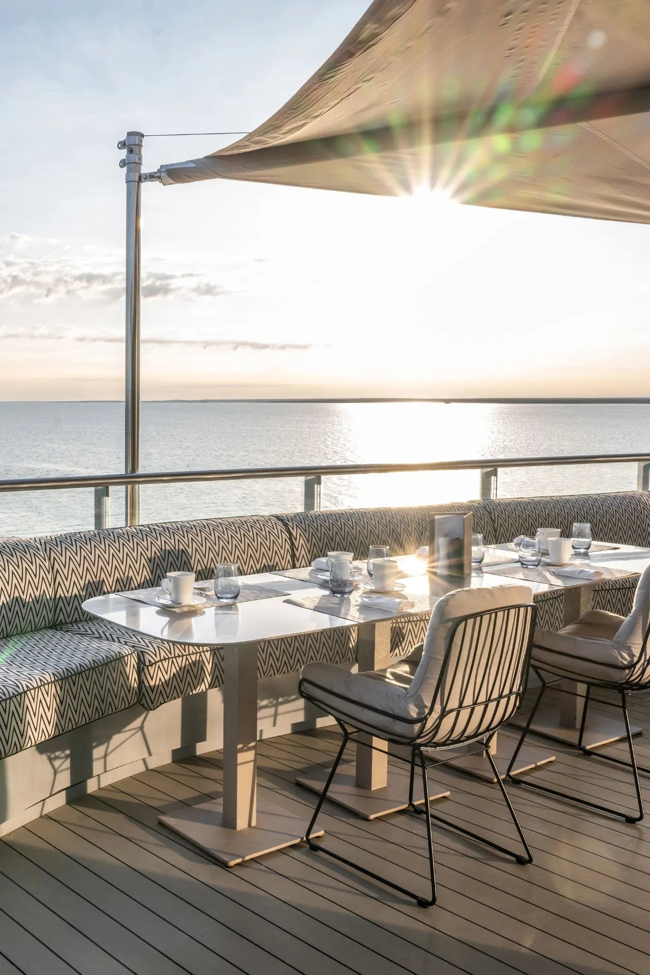 Een elegant buitenrestaurant aan boord biedt een sfeervolle plek om te dineren terwijl de zon langzaam zakt boven de glinsterende zee. Het stijlvolle meubilair, de warme lichtval en het open uitzicht creëren een perfecte ambiance voor ontspannen momenten tijdens een luxe cruise. Deze setting benadrukt de combinatie van verfijnde hospitality en rust die een luxe cruise vakantie zo uniek maakt.