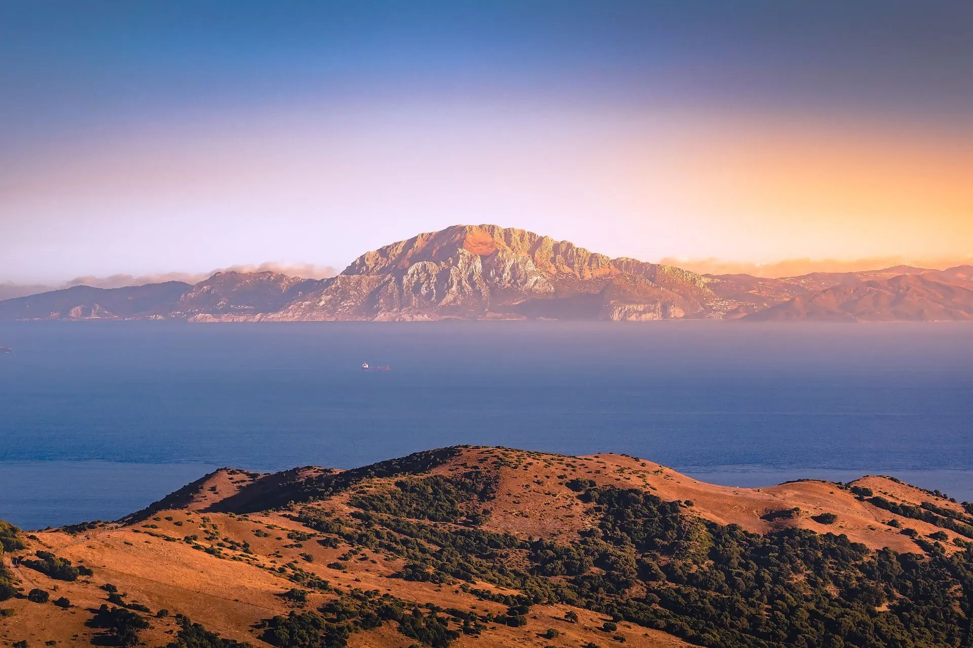 Panoramisch uitzicht op de Straat van Gibraltar, met de rots van Gibraltar aan de ene kant en de kust van Marokko in de verte, onder een helderblauwe lucht.