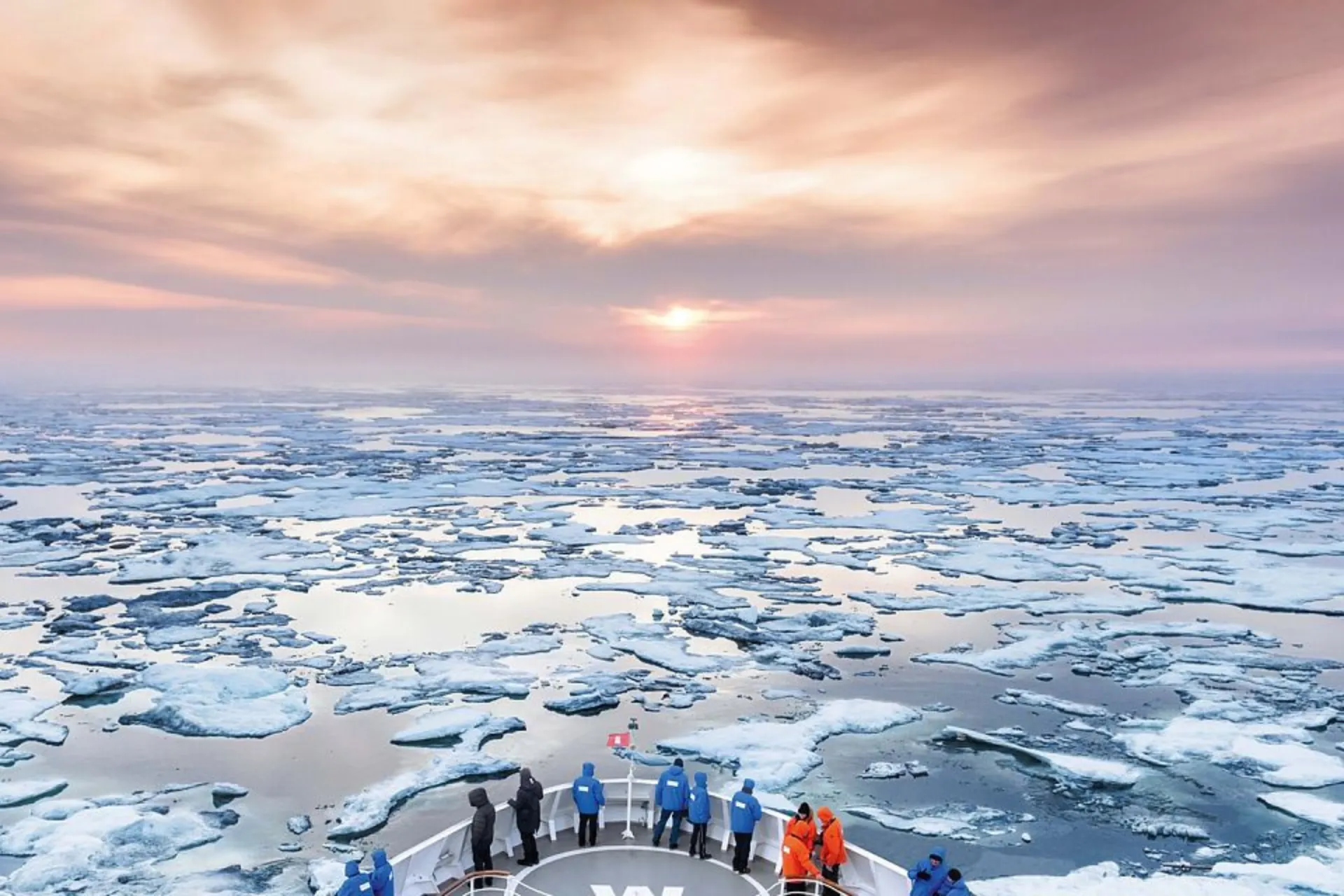 Luchtfoto van een Hapag Lloyd cruiseschip bij zonsondergang, ijsbrekend terwijl mensen op het dek staan en genieten van het uitzicht.