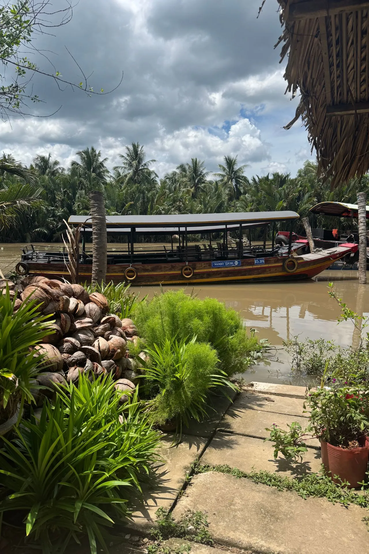 Traditionele houten boot aan de oever van een kanaal in de Mekong Delta, omringd door kokospalmen en tropische begroeiing. Dit waterrijke gebied in Zuid-Vietnam staat bekend om zijn drijvende markten, lokale dorpen en authentieke kennismaking met het Vietnamese leven.