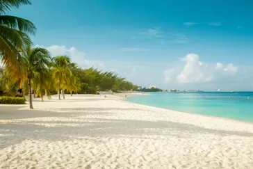 Uitzicht over Seven Mile Beach met wit zand, turquoise water en kleurrijke strandbarretjes langs de kustlijn.