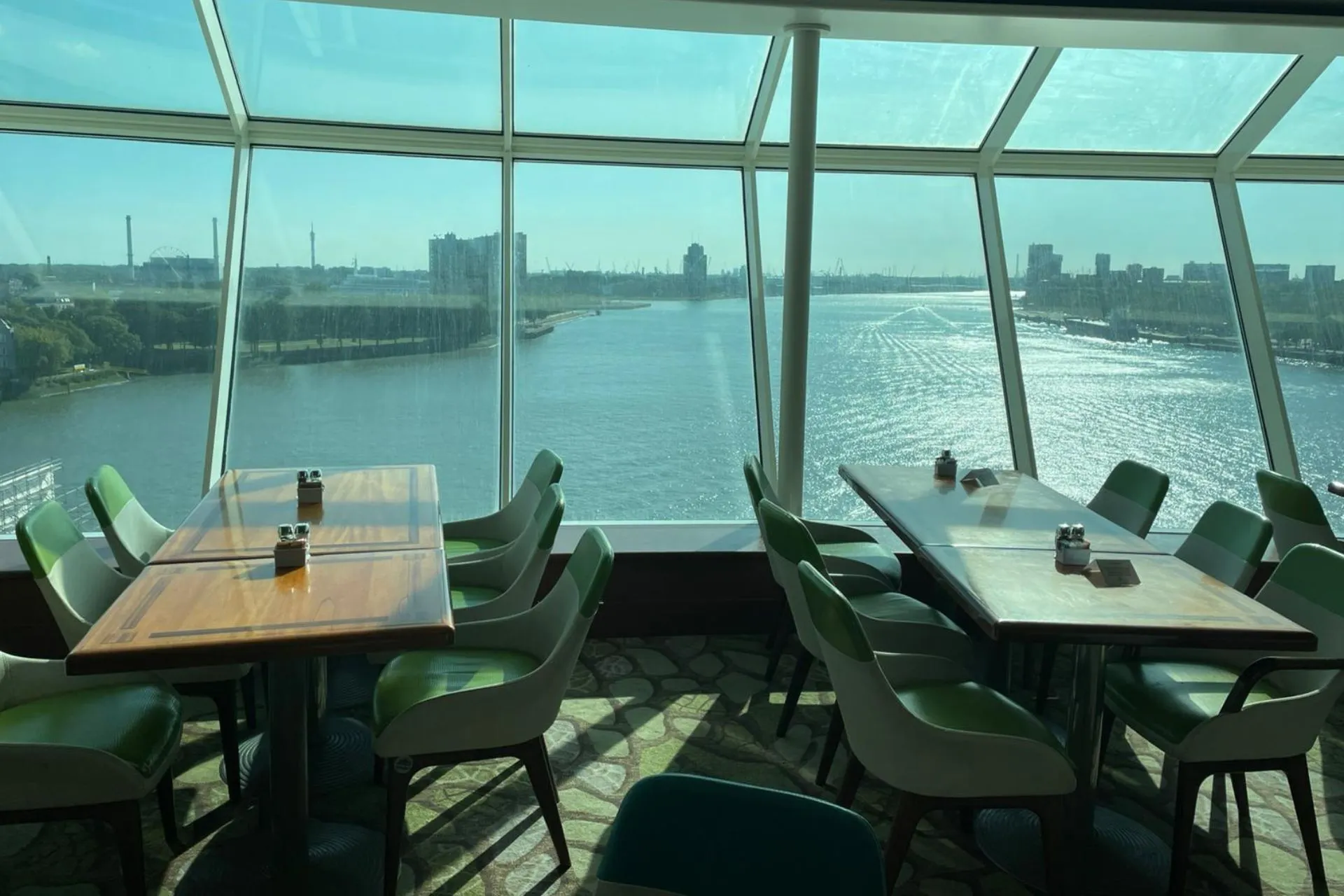 Zitplaatsen bij grote ramen in een restaurant aan boord van de Independence of the Seas, met panoramisch uitzicht over de rivier en skyline.