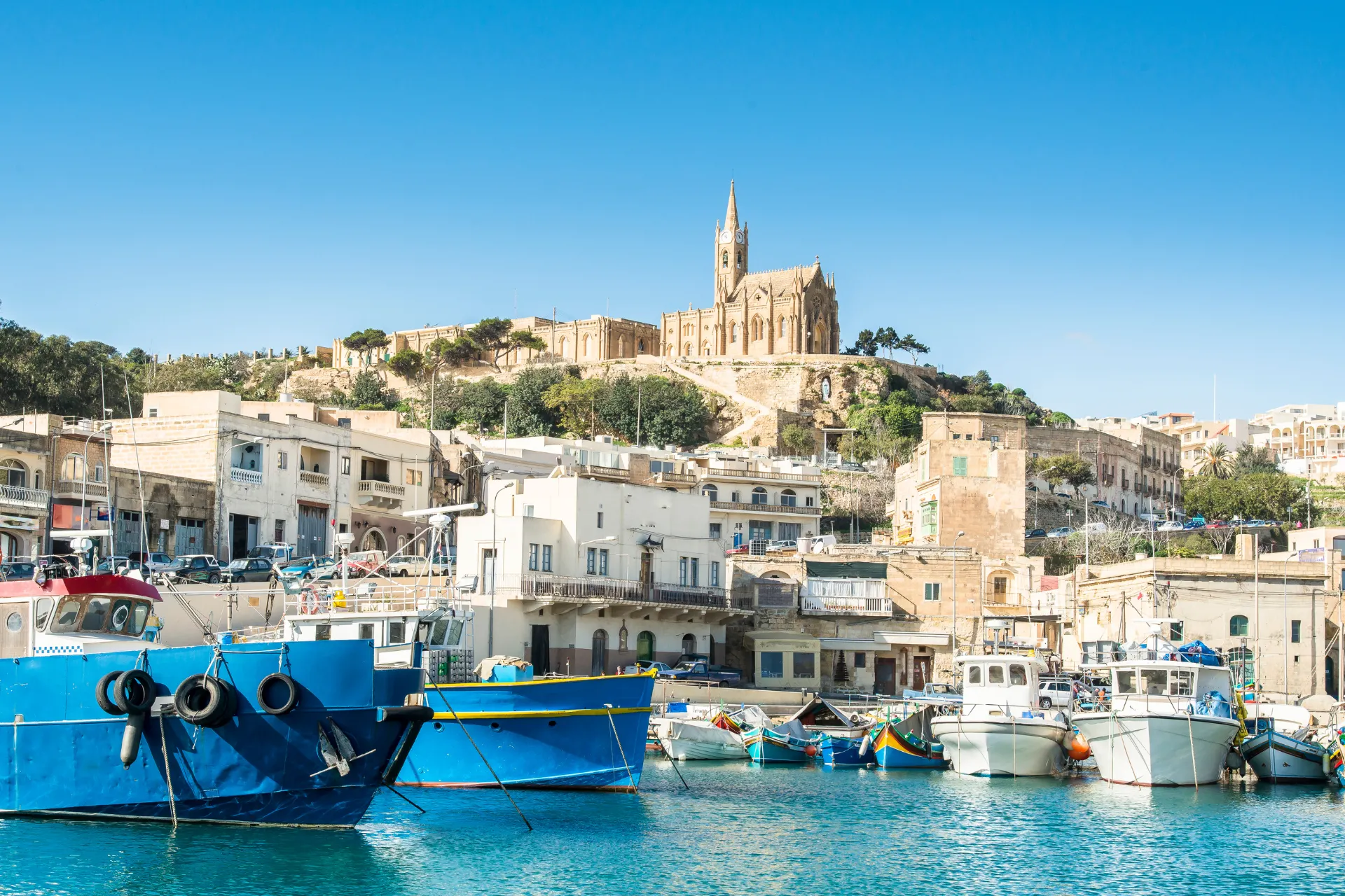 Rustige kust van Gozo, Malta, waar kleurrijke bootjes drijven op kristalhelder water.