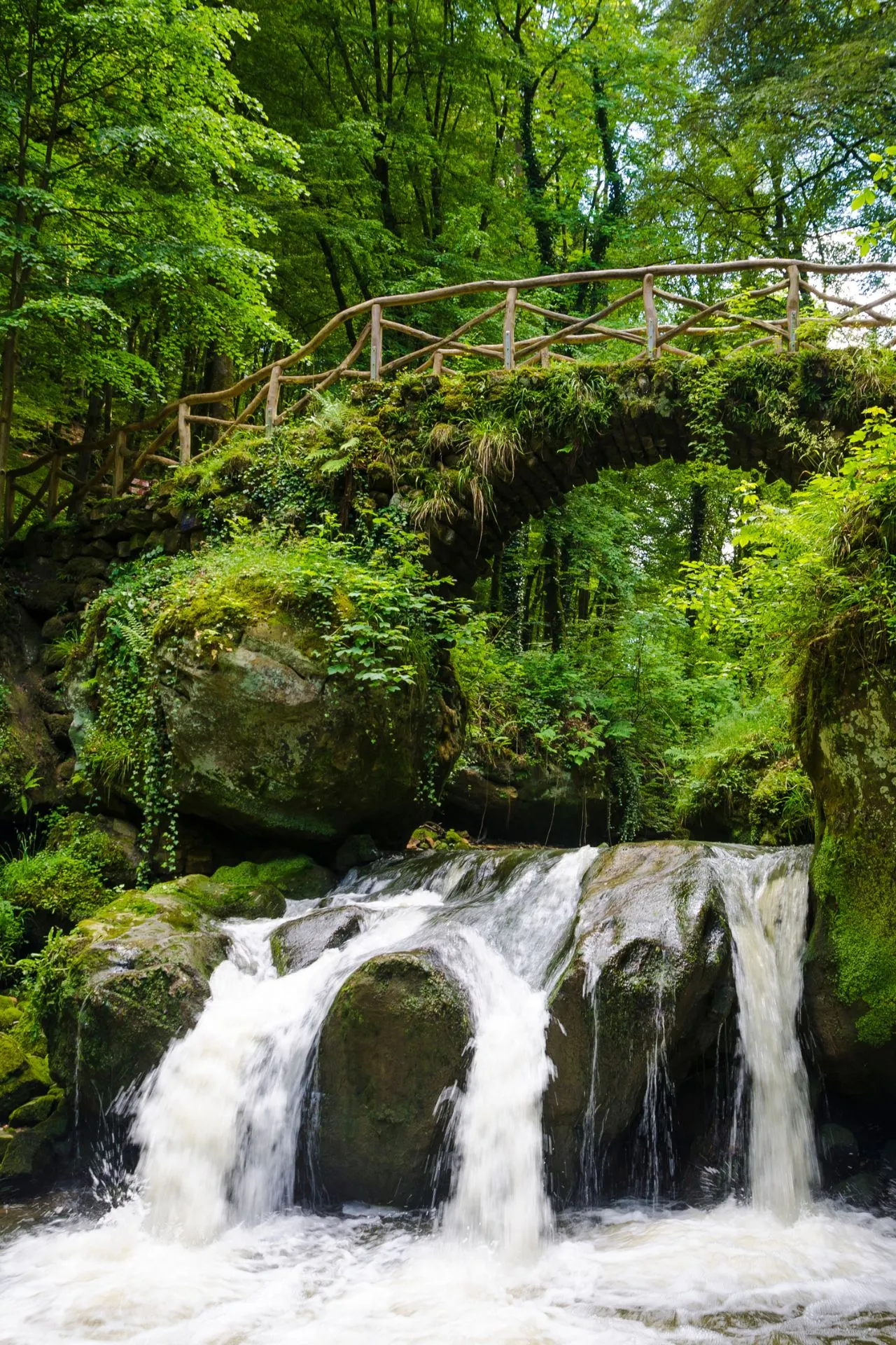 Een schilderachtige houten brug over een kleine waterval omringd door weelderig groen in Müllerthal, Luxemburg