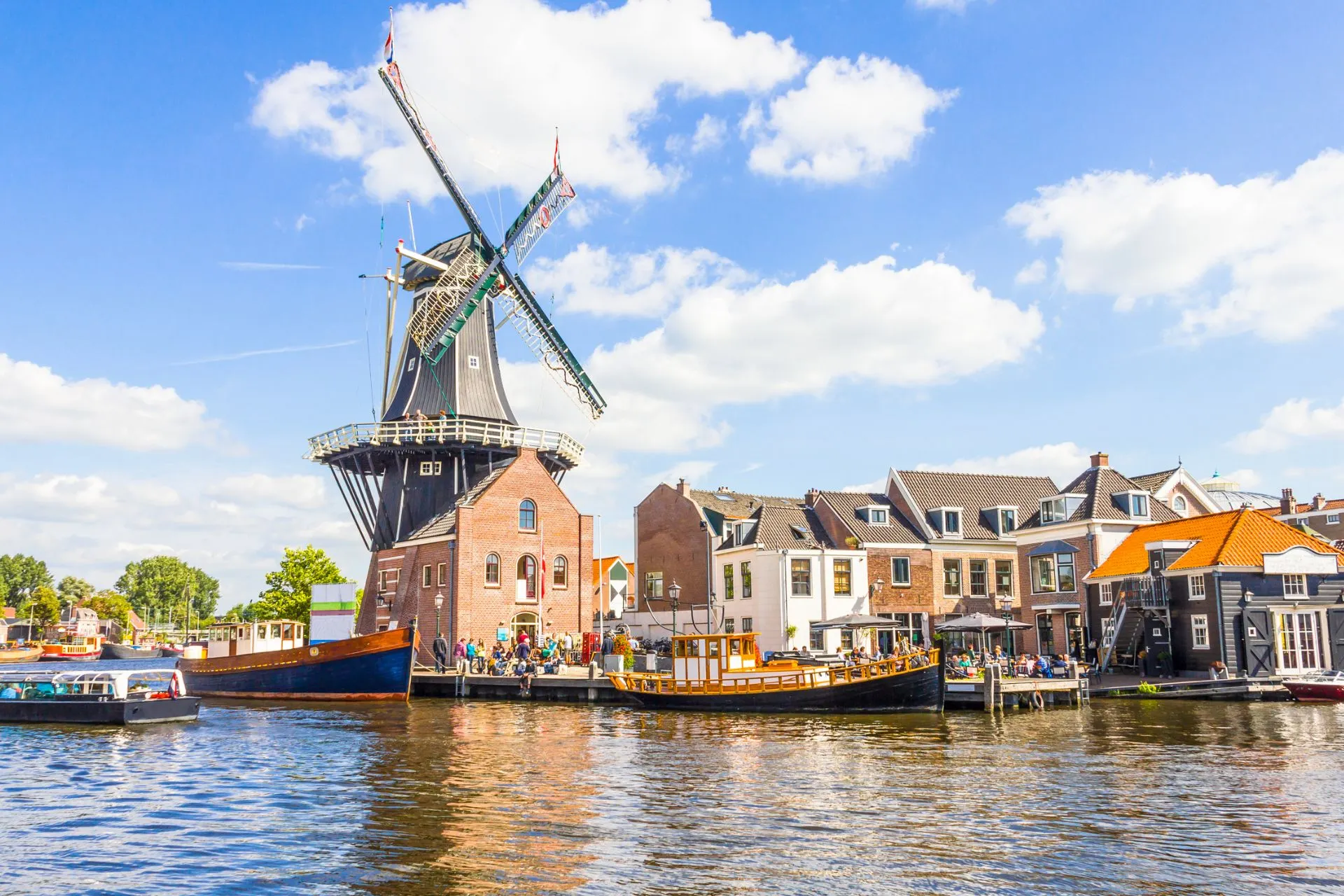 De molen De Adriaan aan het Spaarne in Haarlem op een zonnige dag, met boten in het water en karakteristieke Hollandse huizen op de achtergrond.